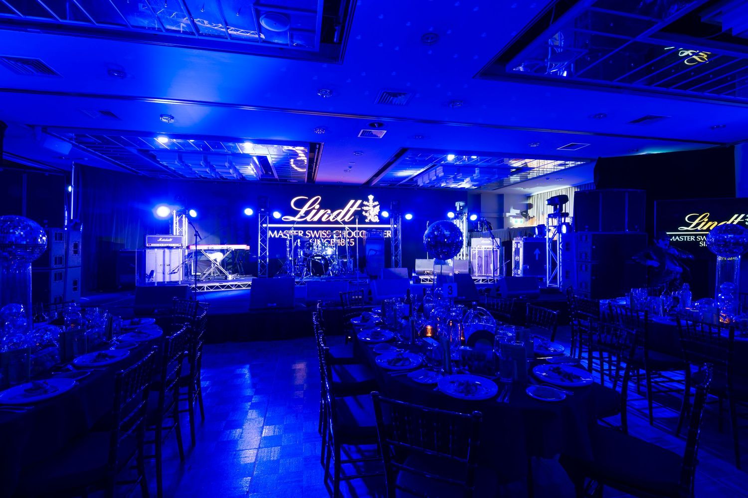 A nightclub interior illuminated in vibrant blue lighting with dance floors and seating areas visible across multiple spaces.