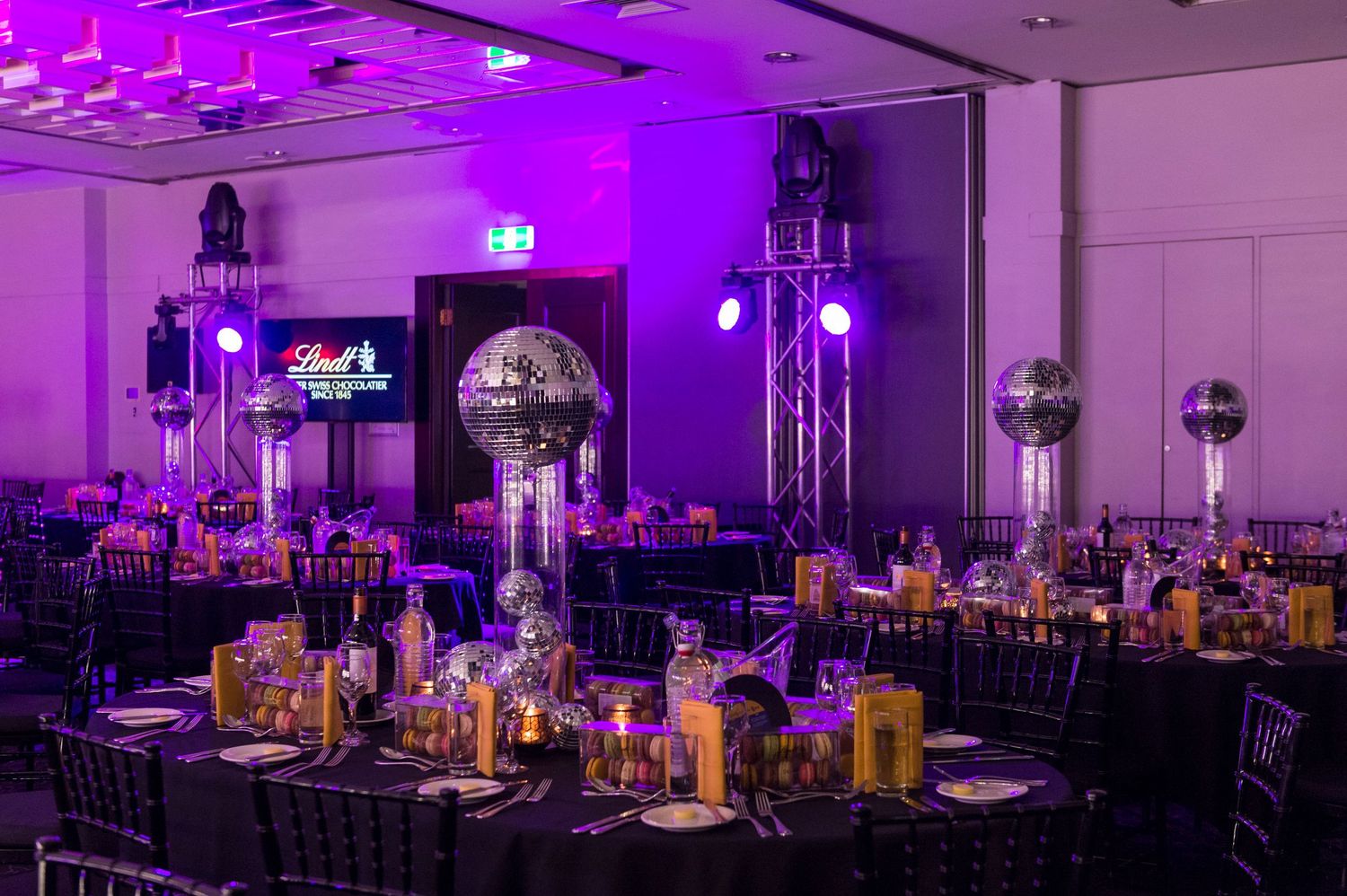 A modern event venue with purple uplighting and elegant table settings for a formal celebration.
