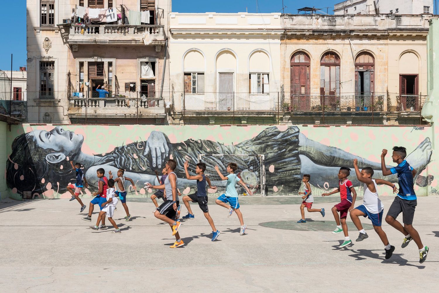 Children playing soccer on a street in front of historic buildings.