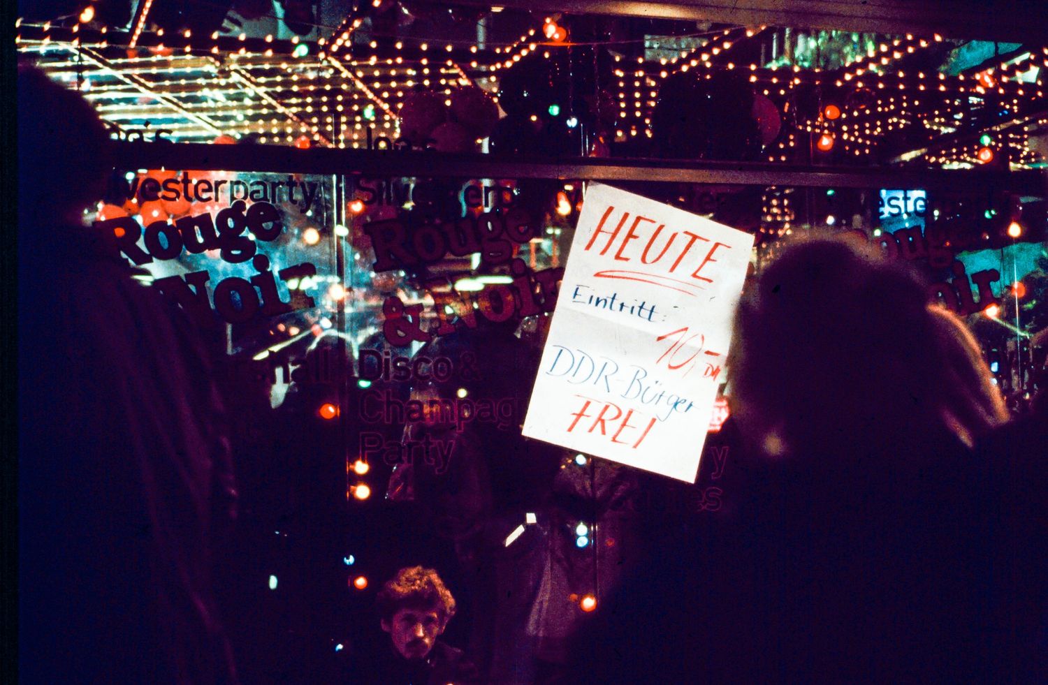 Illuminated nightclub scene with colorful string lights and a sign reading 