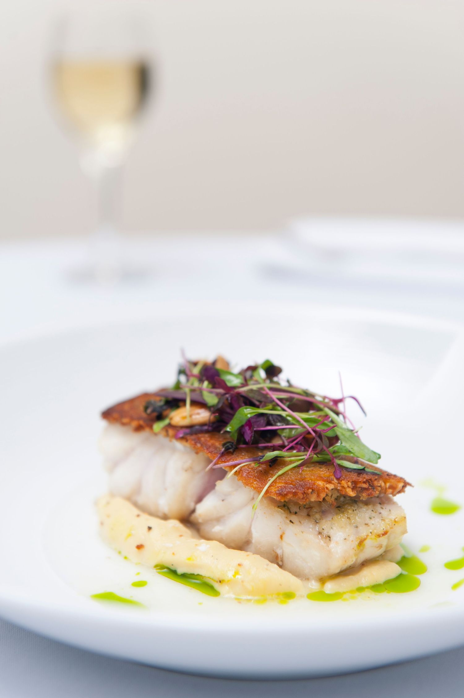 Crispy-skinned fish dish garnished with purple microgreens on white porcelain plate.