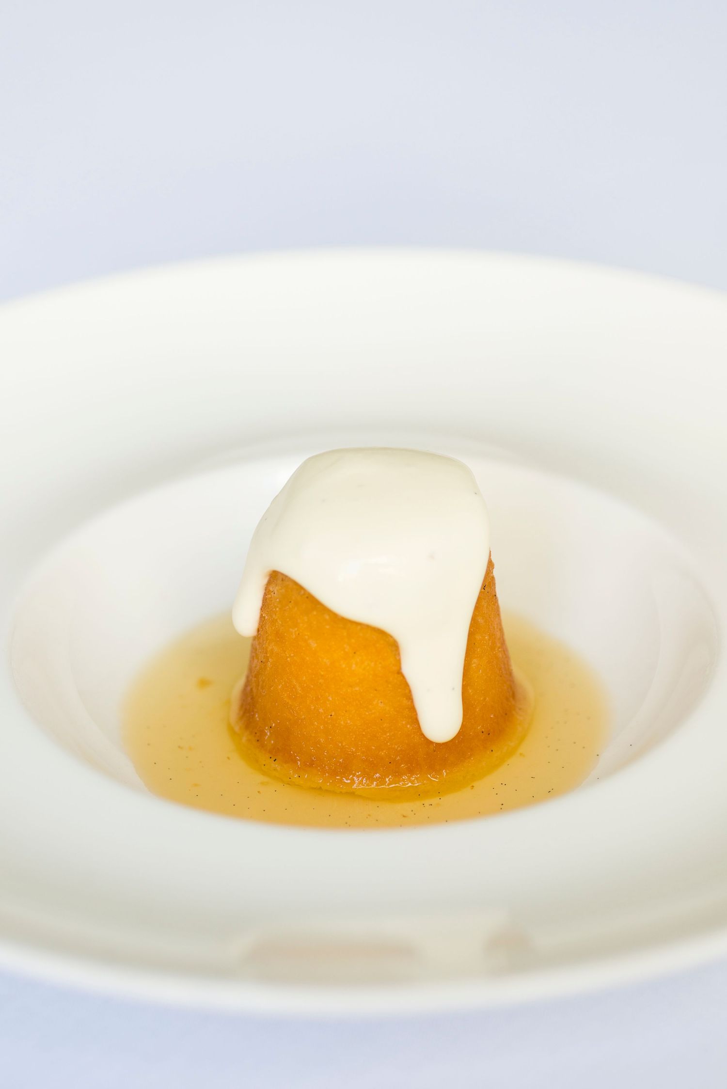 Small orange dessert pudding with white cream sauce in an elegant white bowl.