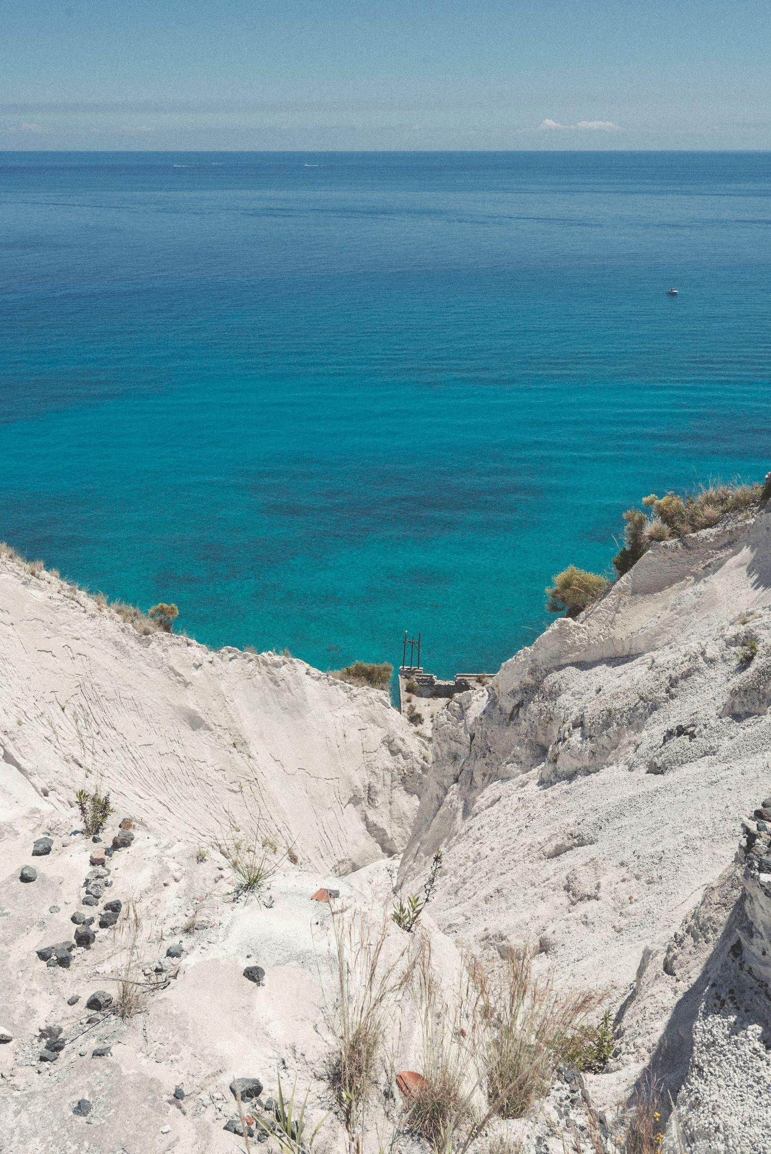 White chalk cliffs overlook crystal clear turquoise Mediterranean waters on a sunny day with blue skies.