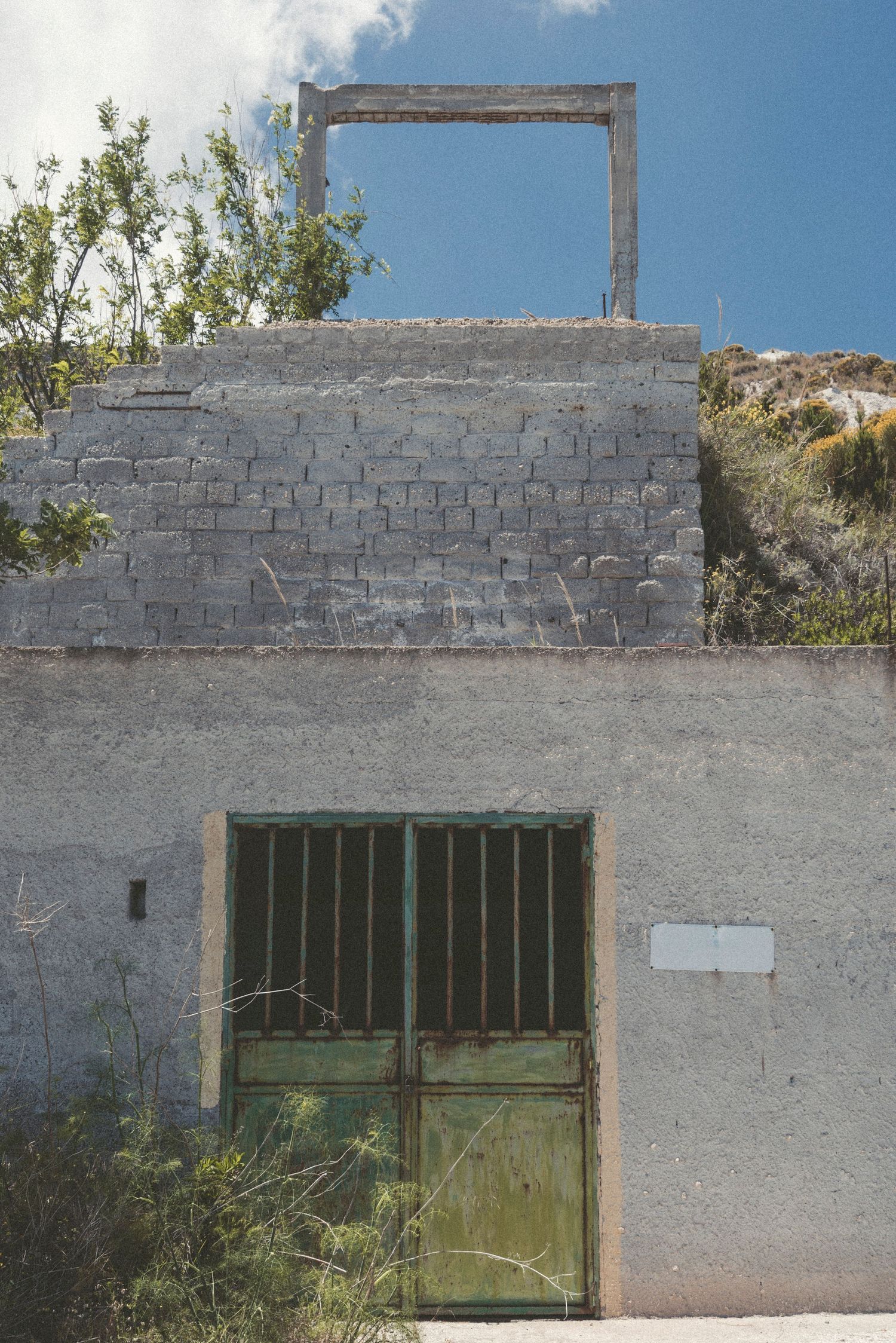 Old weathered stone wall with three green barred windows and rustic architectural details against a blue sky.