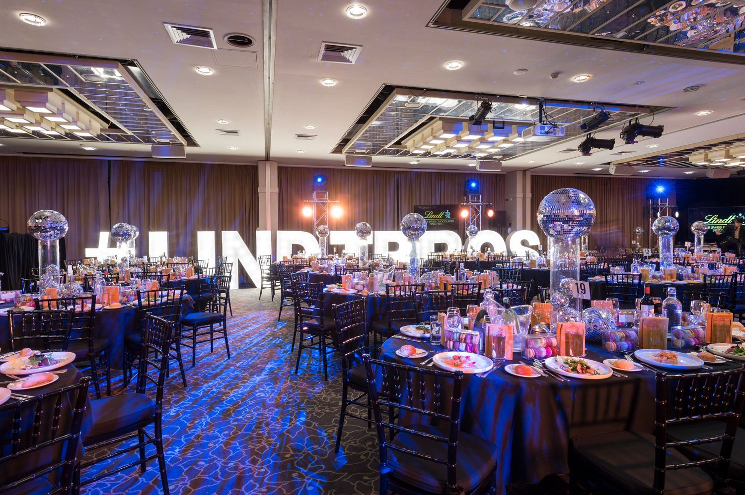 Elegant banquet hall setup with blue uplighting, dark chairs, and round tables decorated for a formal event.