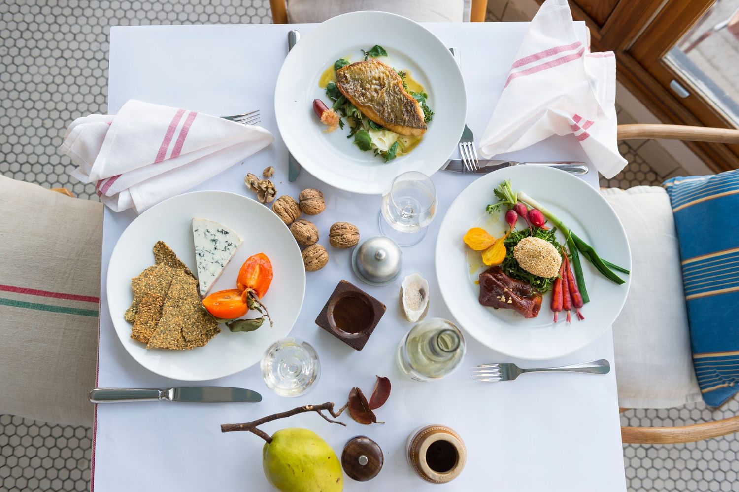 Overhead view of multiple plates with appetizers and wine glasses on white tablecloth.