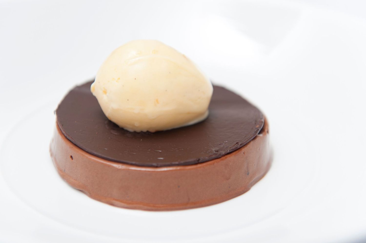 Chocolate dessert discs topped with light cream dollops arranged in a row on white plates.