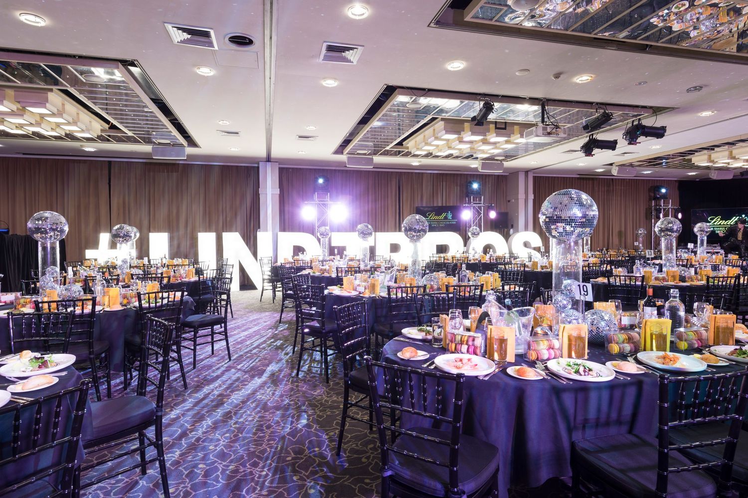 Large banquet hall decorated with purple uplighting and elegant table settings for a formal event.