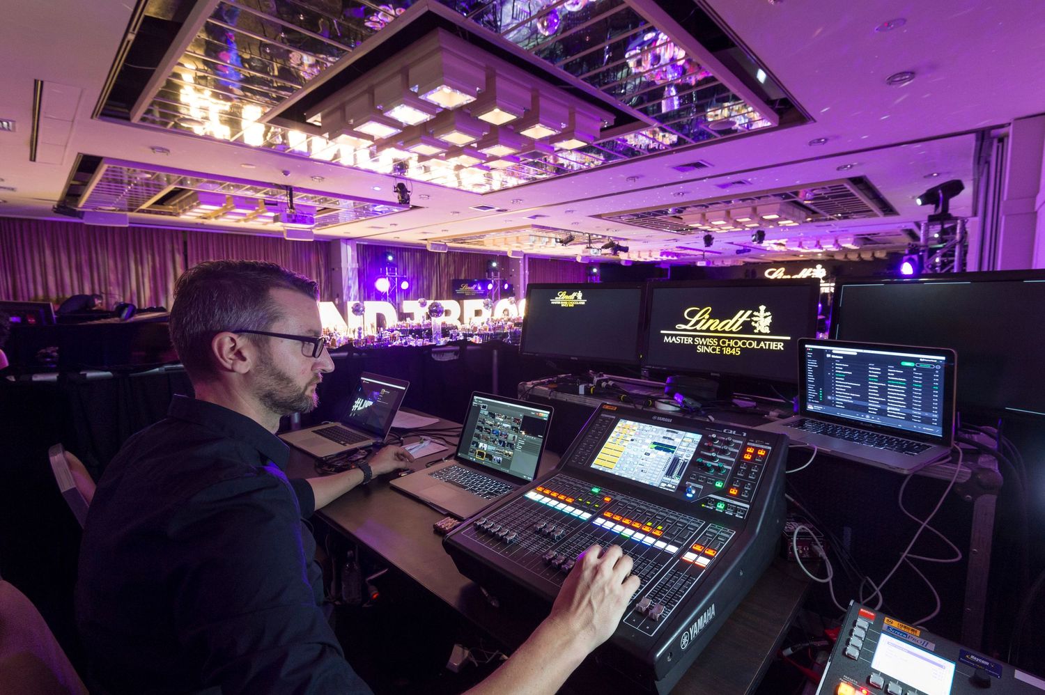 Purple-lit production control room with multiple monitors and equipment showing live broadcast setup.
