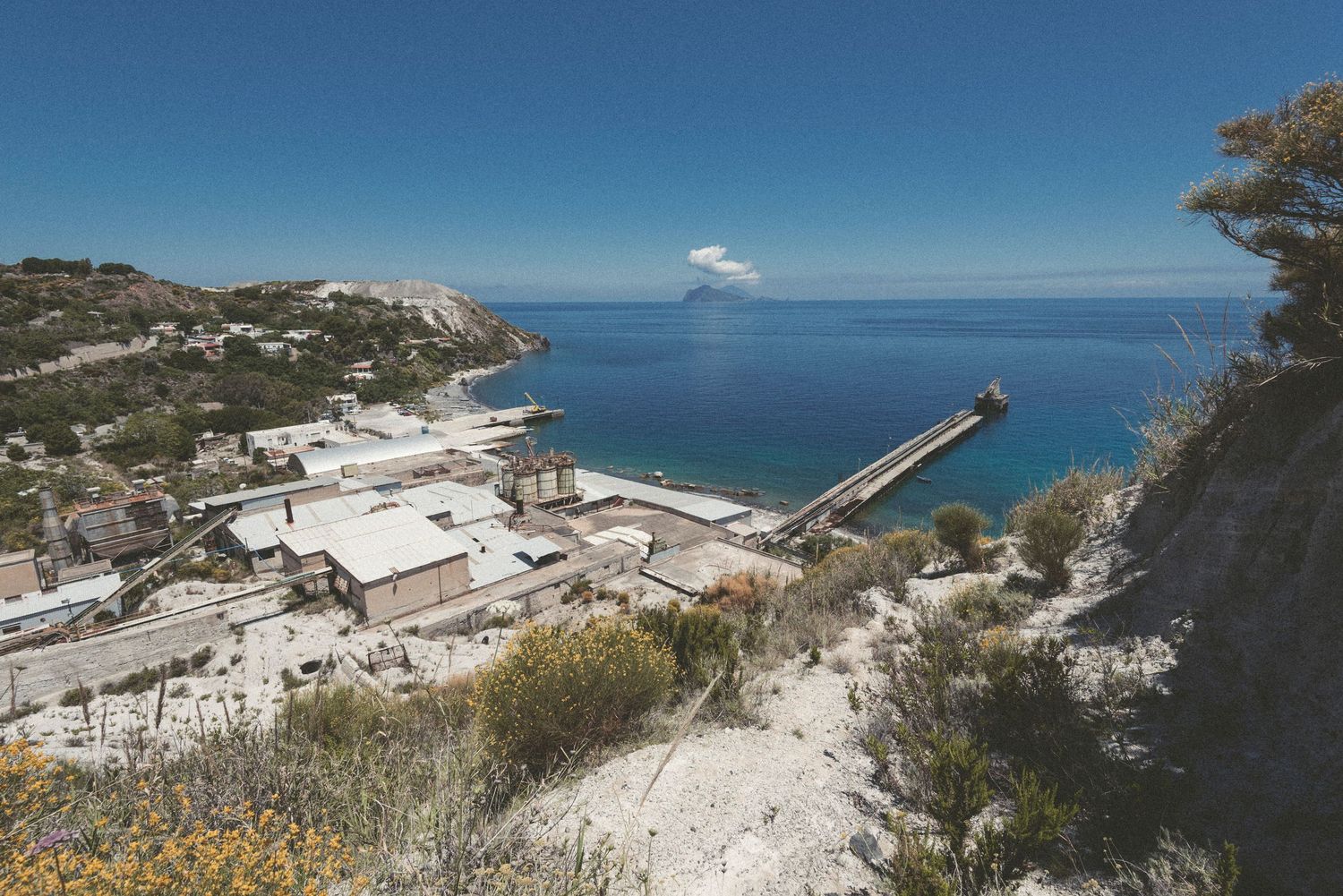 Aerial view of a coastal quarry operation with white stone deposits and processing facilities near the ocean.
