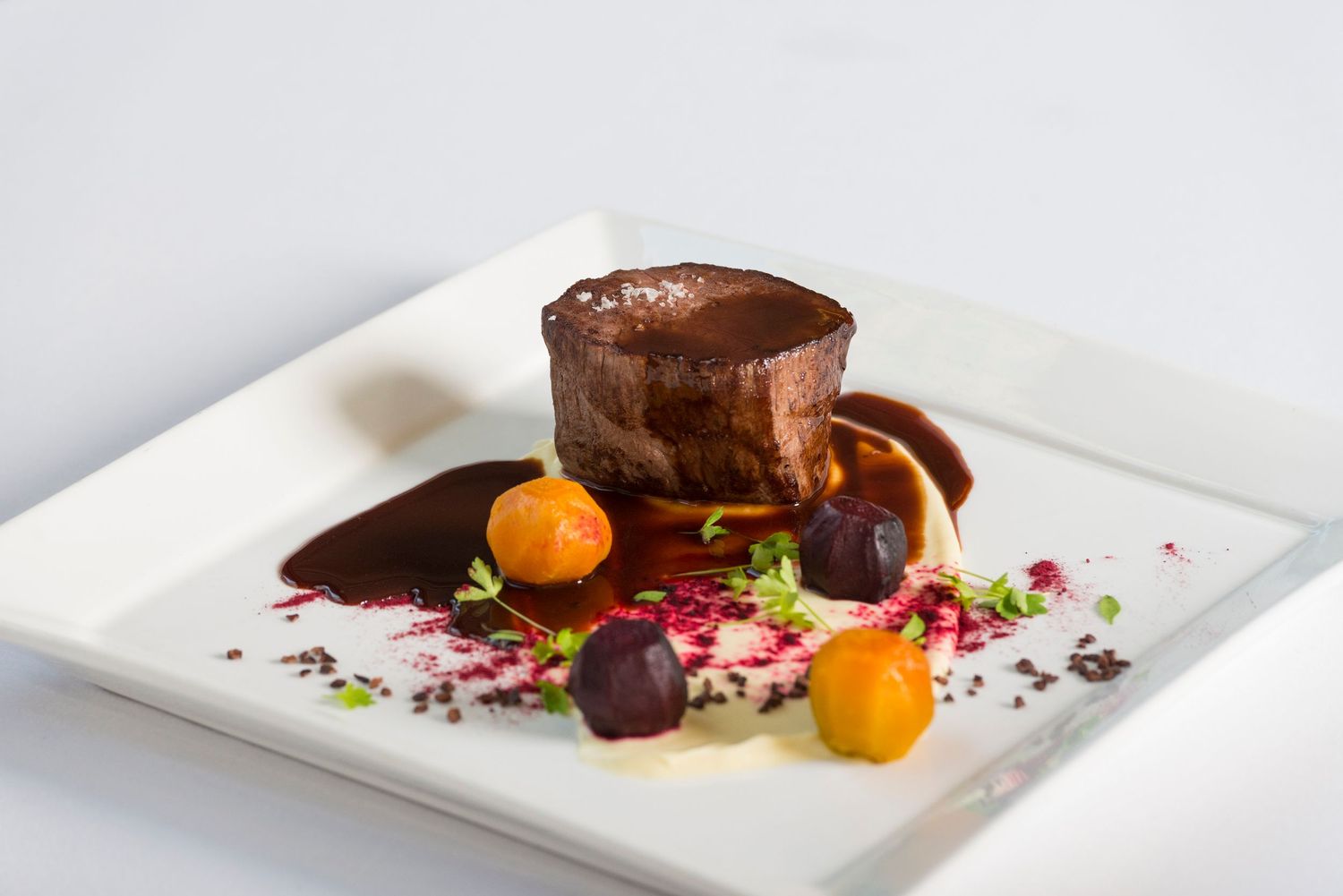 Gourmet beef tenderloin with citrus garnish and chocolate elements on white plate.