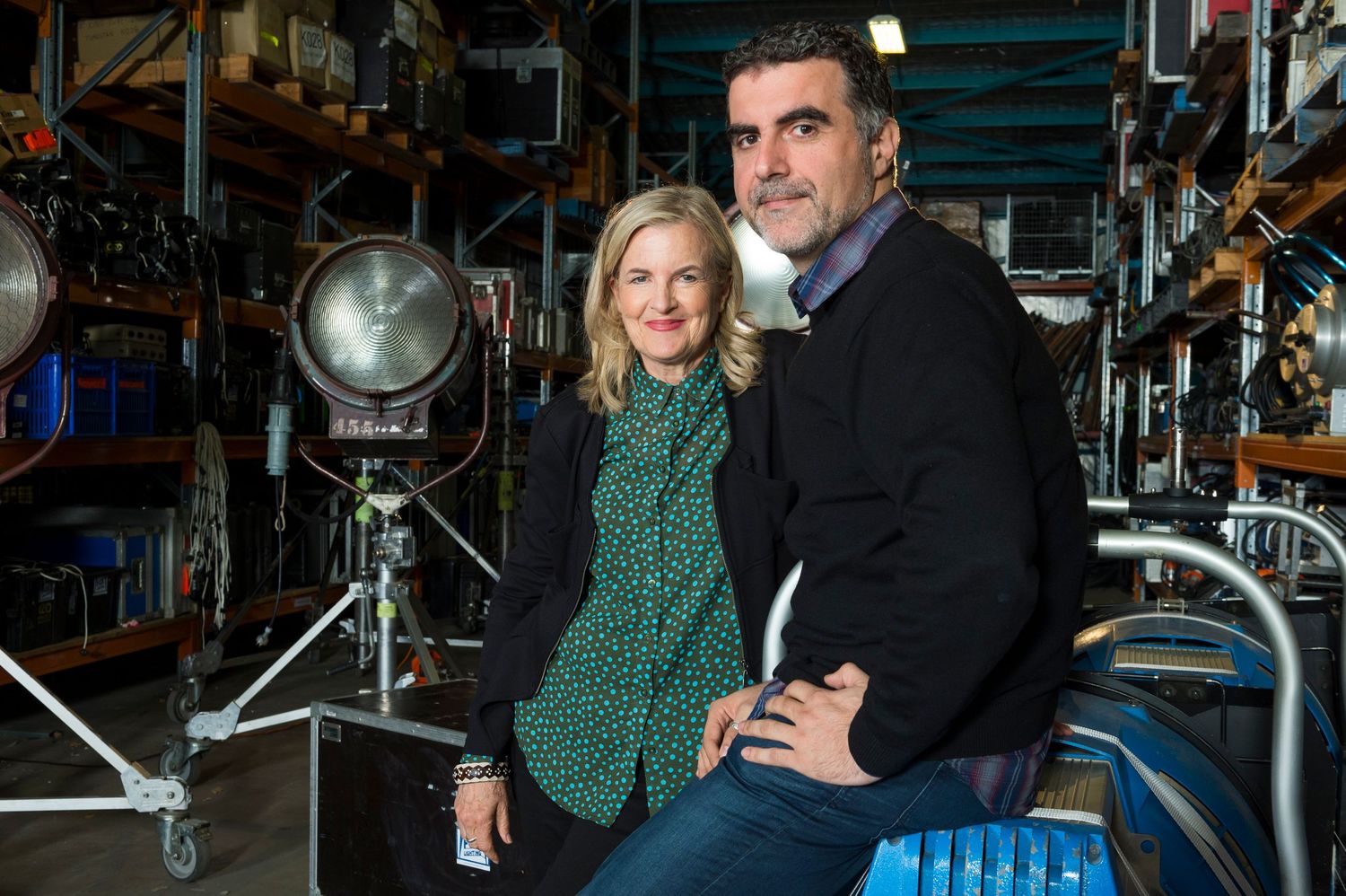 People posing among film production equipment and lighting in a warehouse setting.