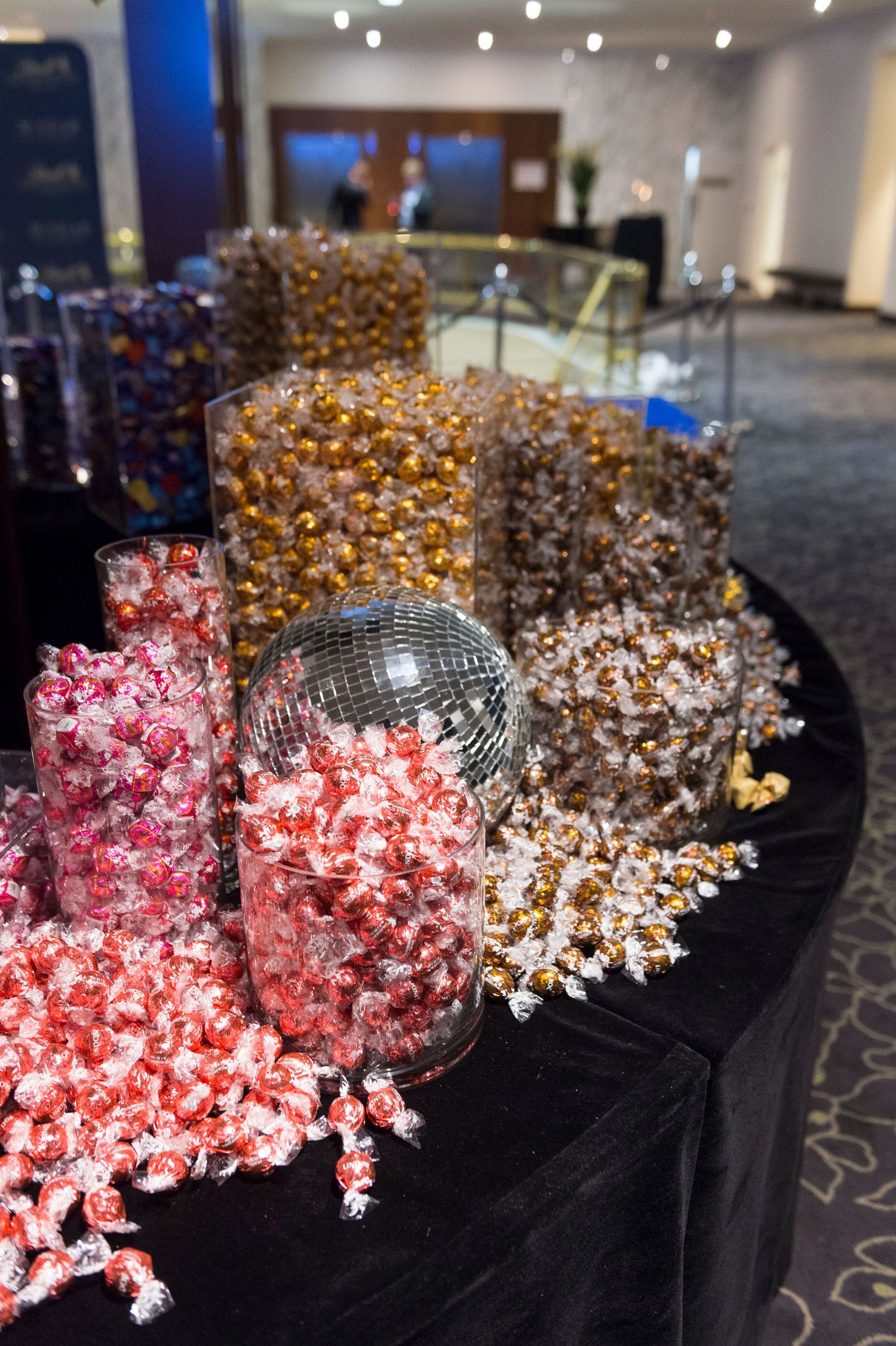 A disco ball centerpiece surrounded by pink and gold popcorn decorations on a black tablecloth at an event.