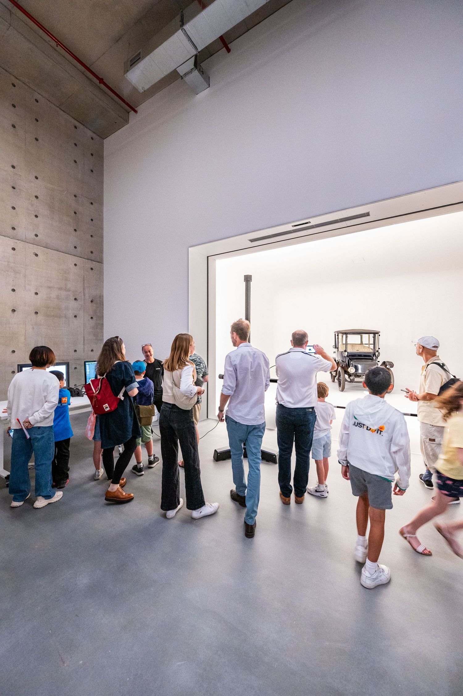 Group of visitors exploring a minimalist gallery space with white walls and concrete floor.