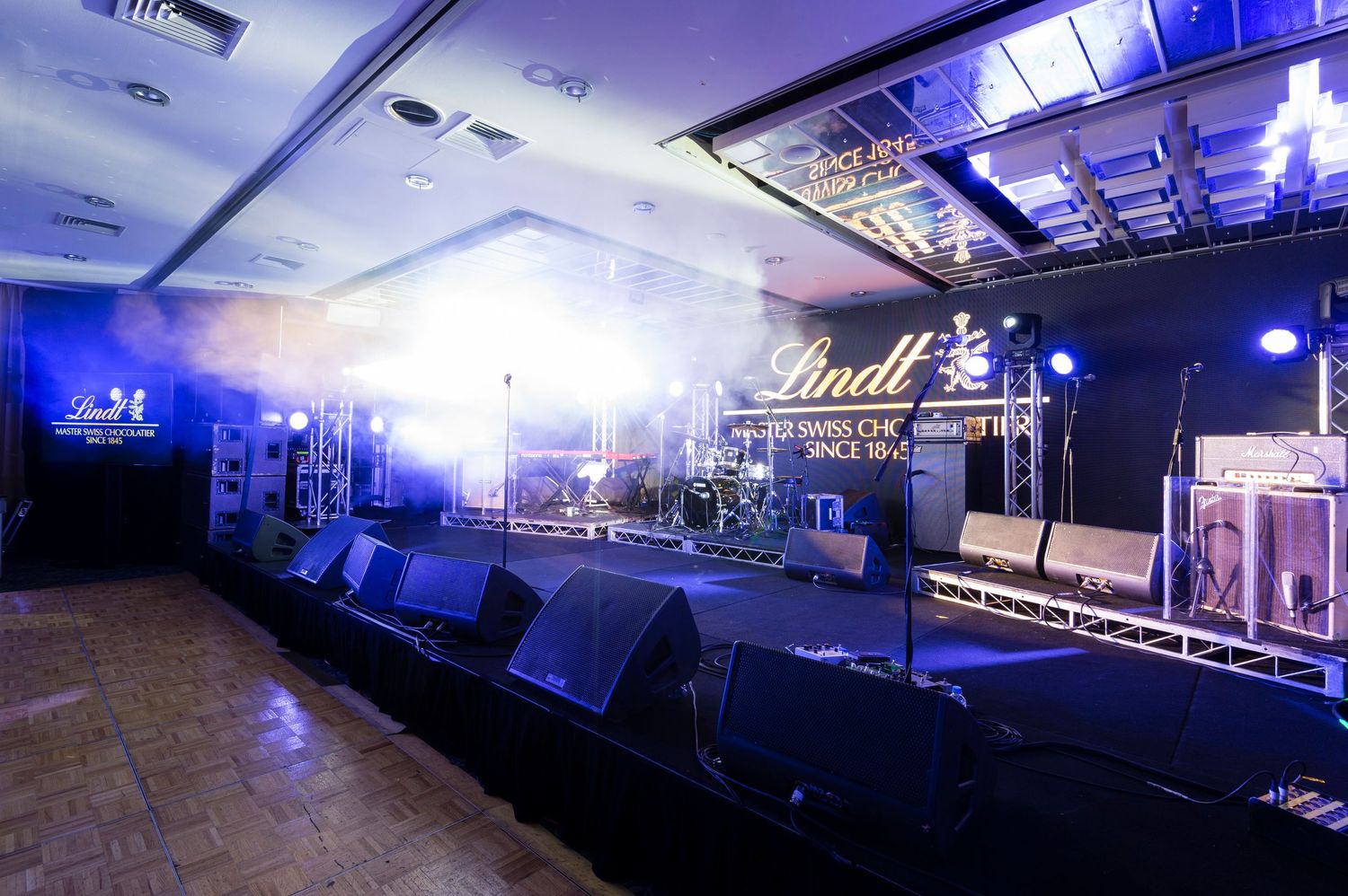 Concert venue interior with blue stage lighting and professional audio equipment setup illuminated in dramatic atmosphere.