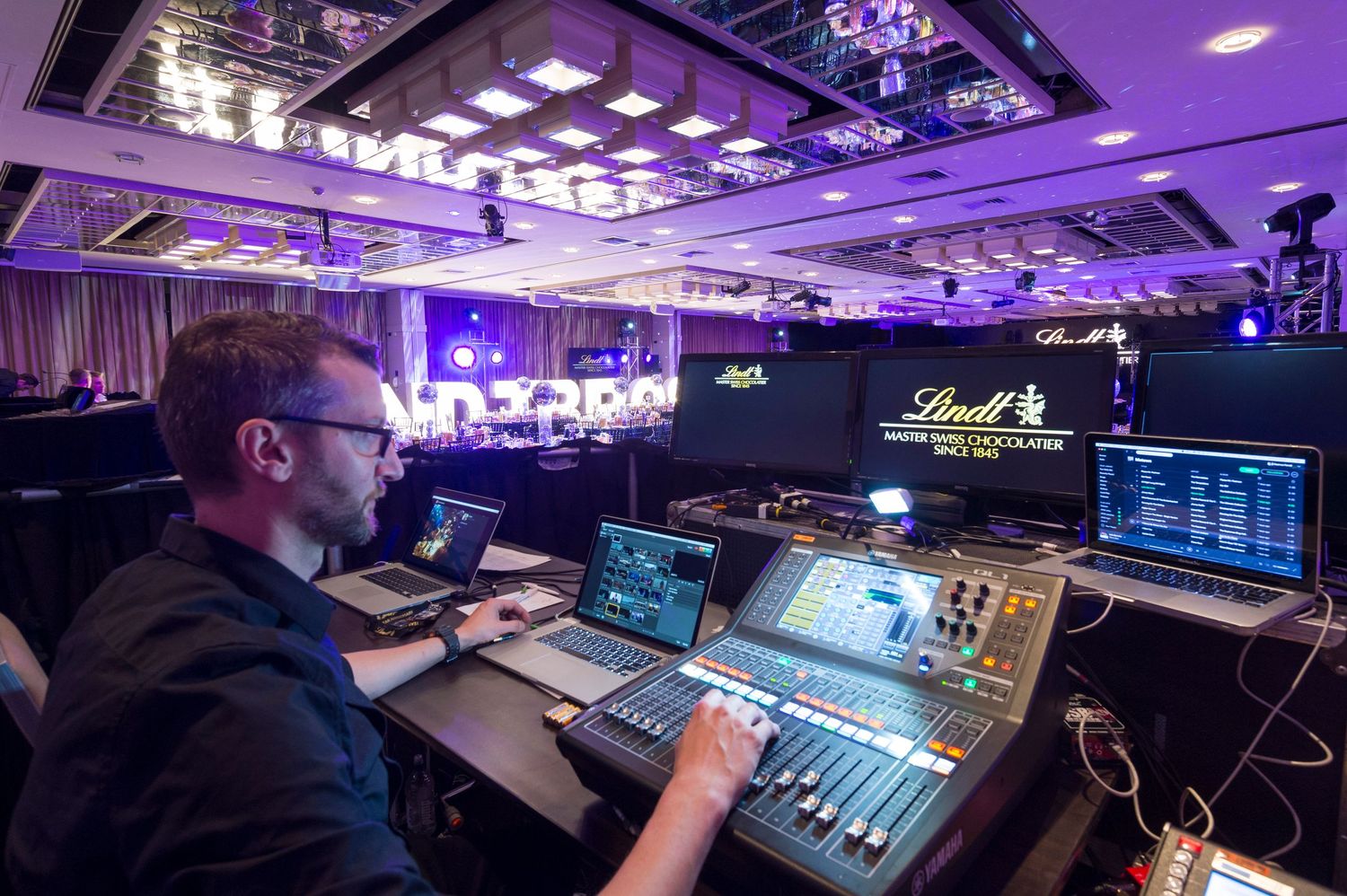 Audio technician operating a digital mixing console with purple lighting in a professional studio environment.