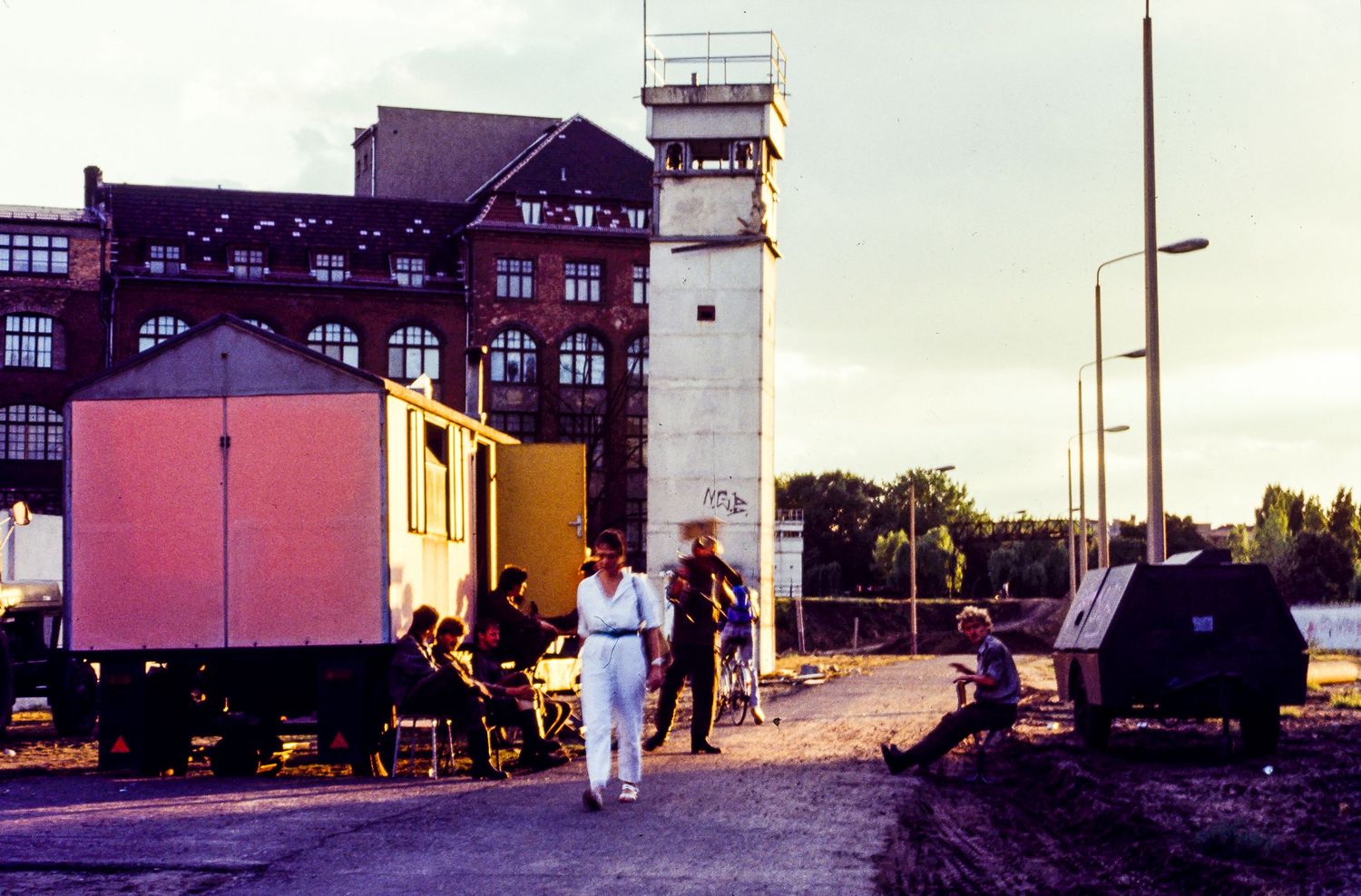 Guard tower and buildings along the Berlin Wall with a pink-colored structure in the foreground.