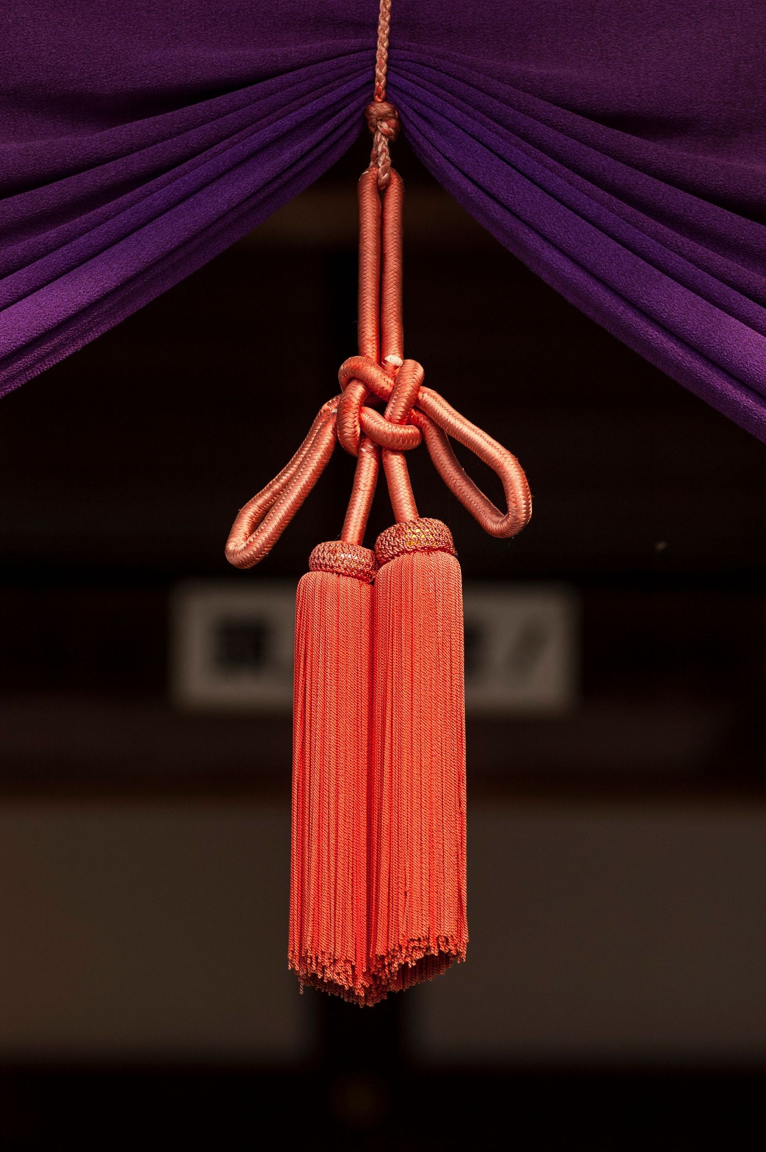 Orange ceremonial tassel hanging from purple fabric in traditional Japanese temple decor.