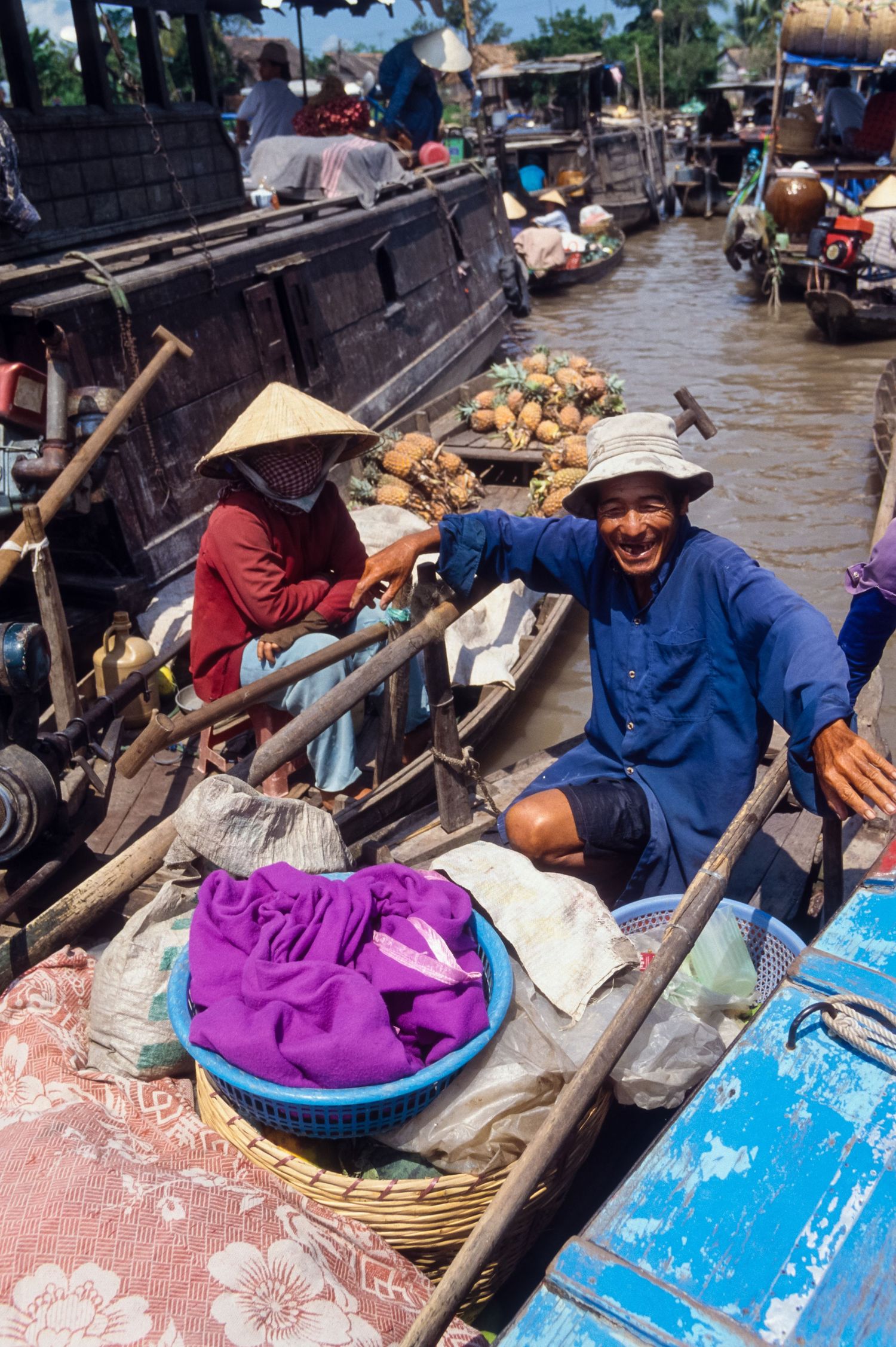 Vendors in traditional conical hats sell goods from wooden boats at an Asian floating market.