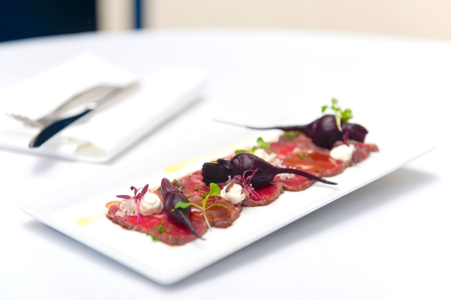 Thinly sliced red meat dish artistically presented with dark sauce and garnishes.