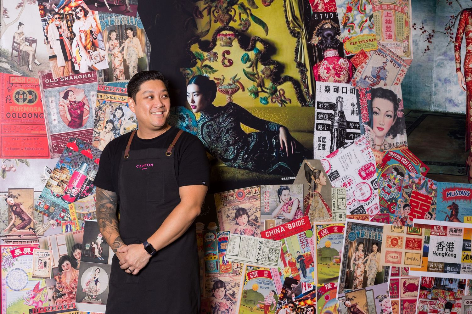 Person in black t-shirt stands against wall covered in colorful Asian posters and artwork.