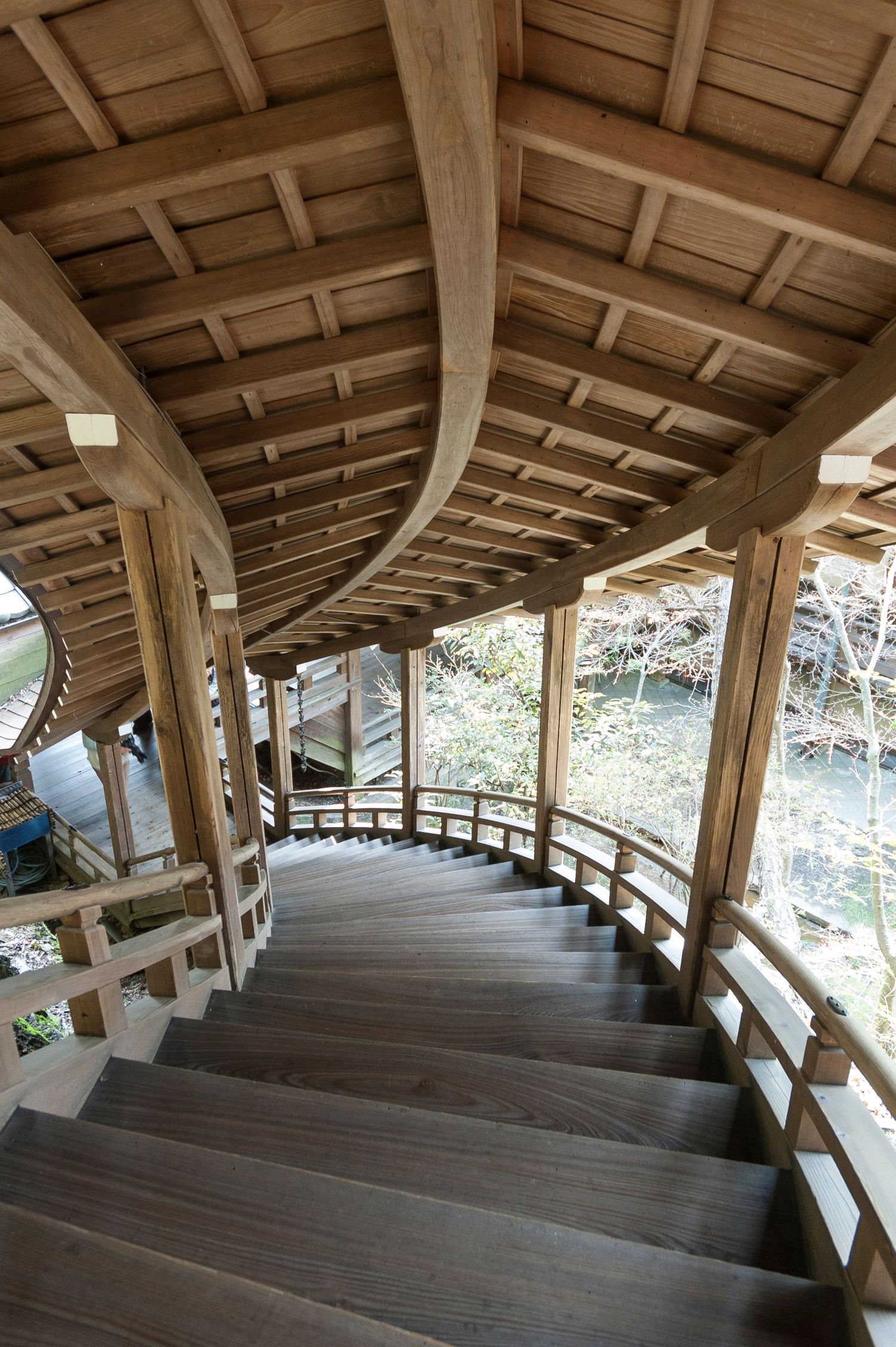 Wooden covered staircase with traditional Japanese architecture descending through a forested area.