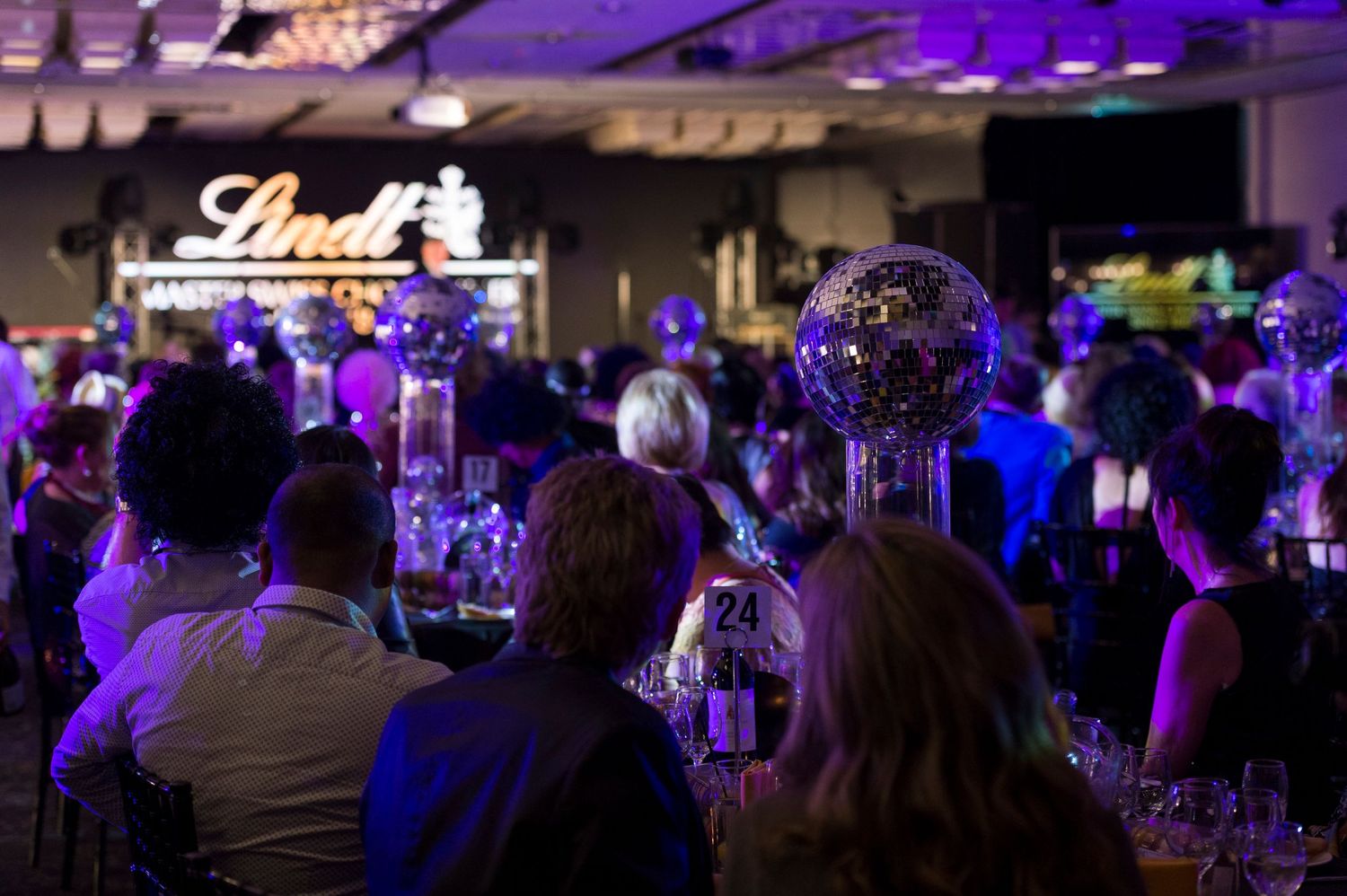 A dimly lit event space with purple lighting and guests seated at round tables during an evening function.