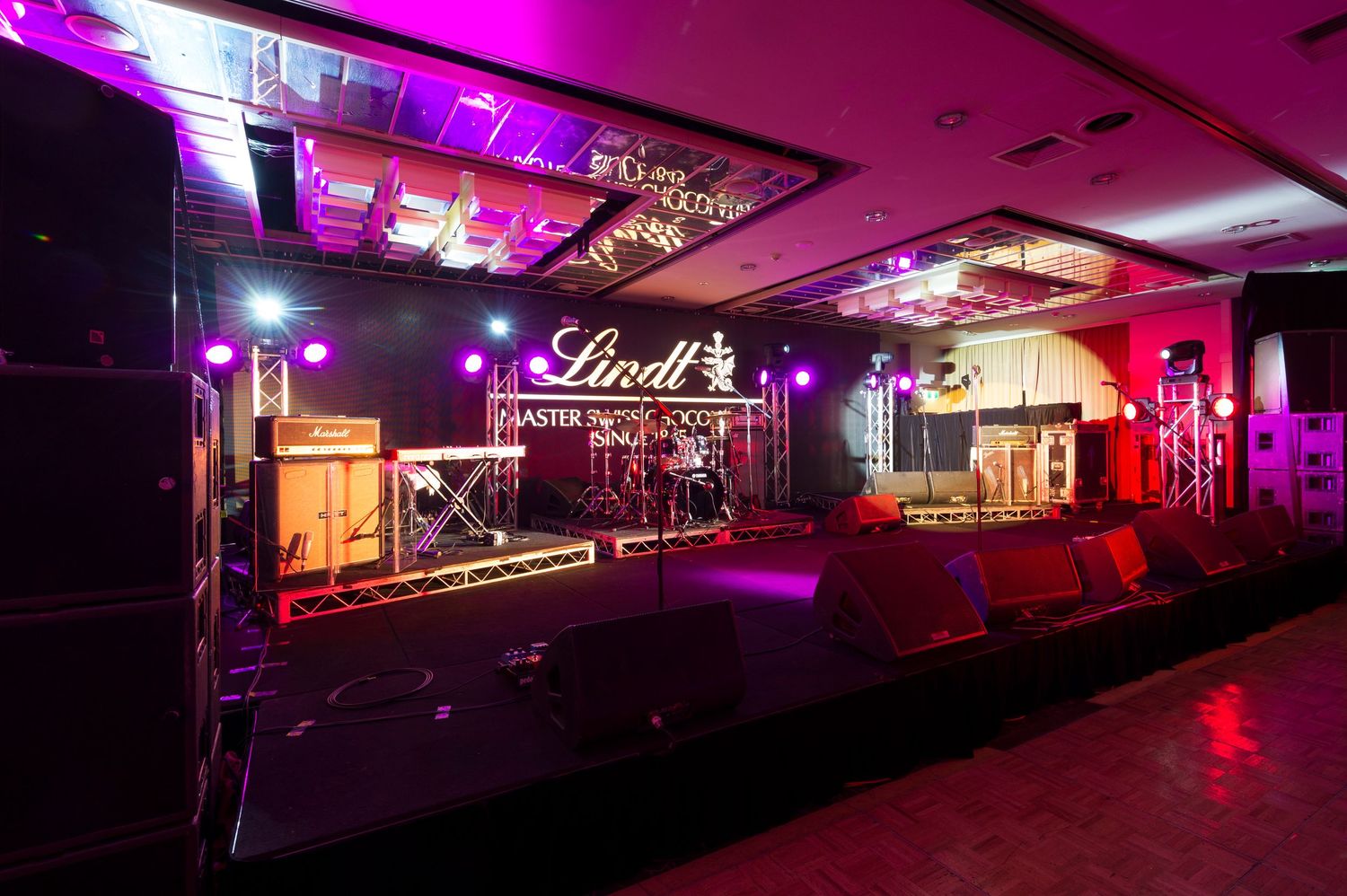 Panoramic view of a nightclub interior with purple and red LED lighting illuminating the empty dance floor and seating area.