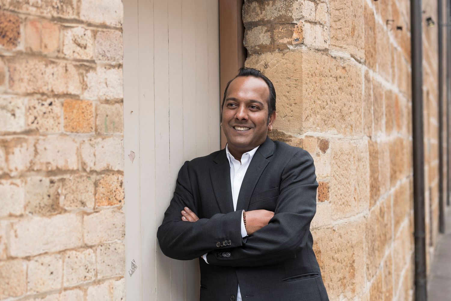 Professional in dark suit smiles while posing against stone wall.