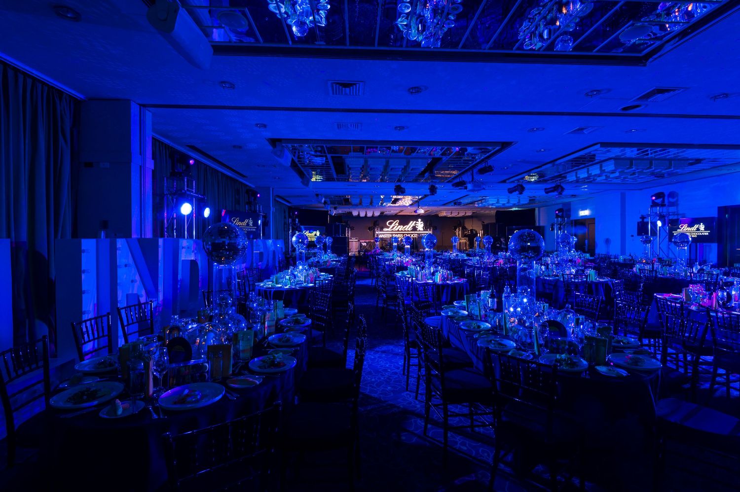 A series of dark blue-lit interior shots showing a dimly illuminated banquet hall or event space setup.