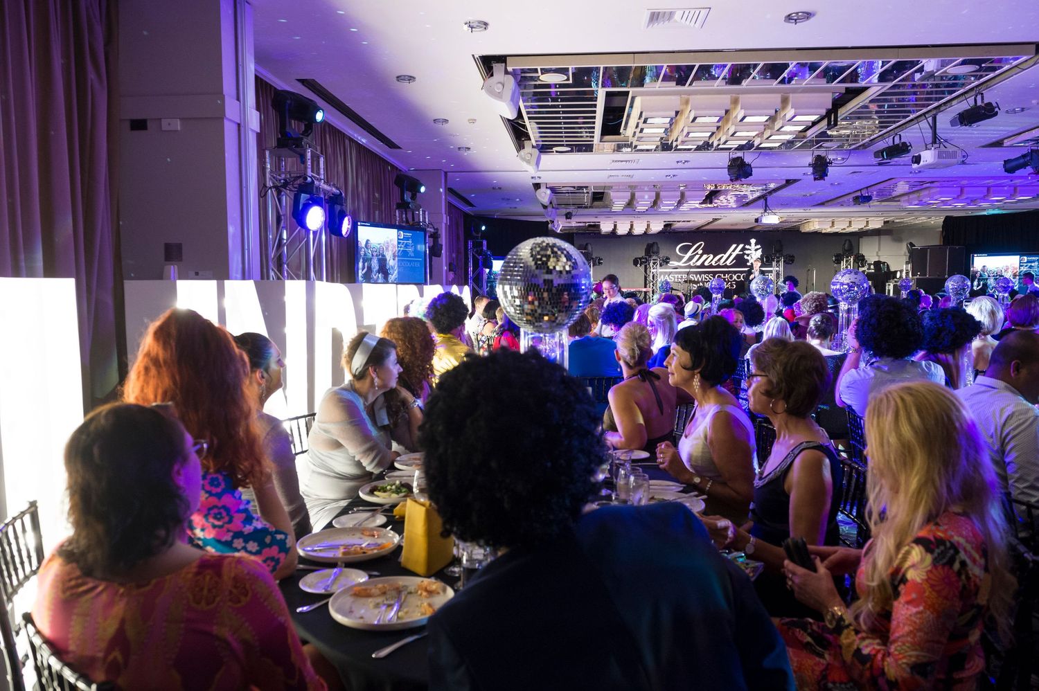 A crowded restaurant dining room with purple mood lighting and people seated at tables along the walls.