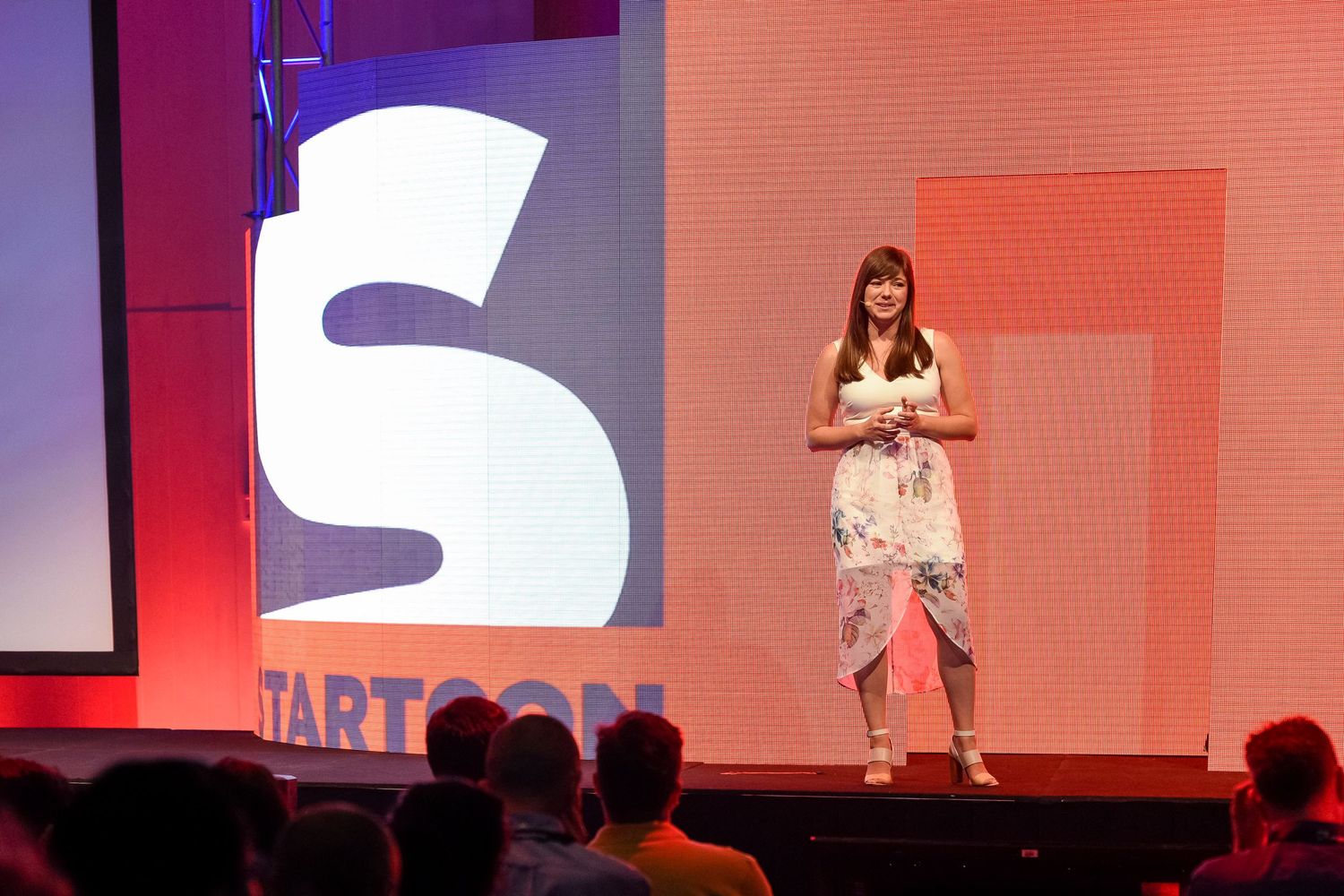 Presenter stands on stage with large start-up logo and red backdrop during conference talk at the Sydney Royal Randwick.