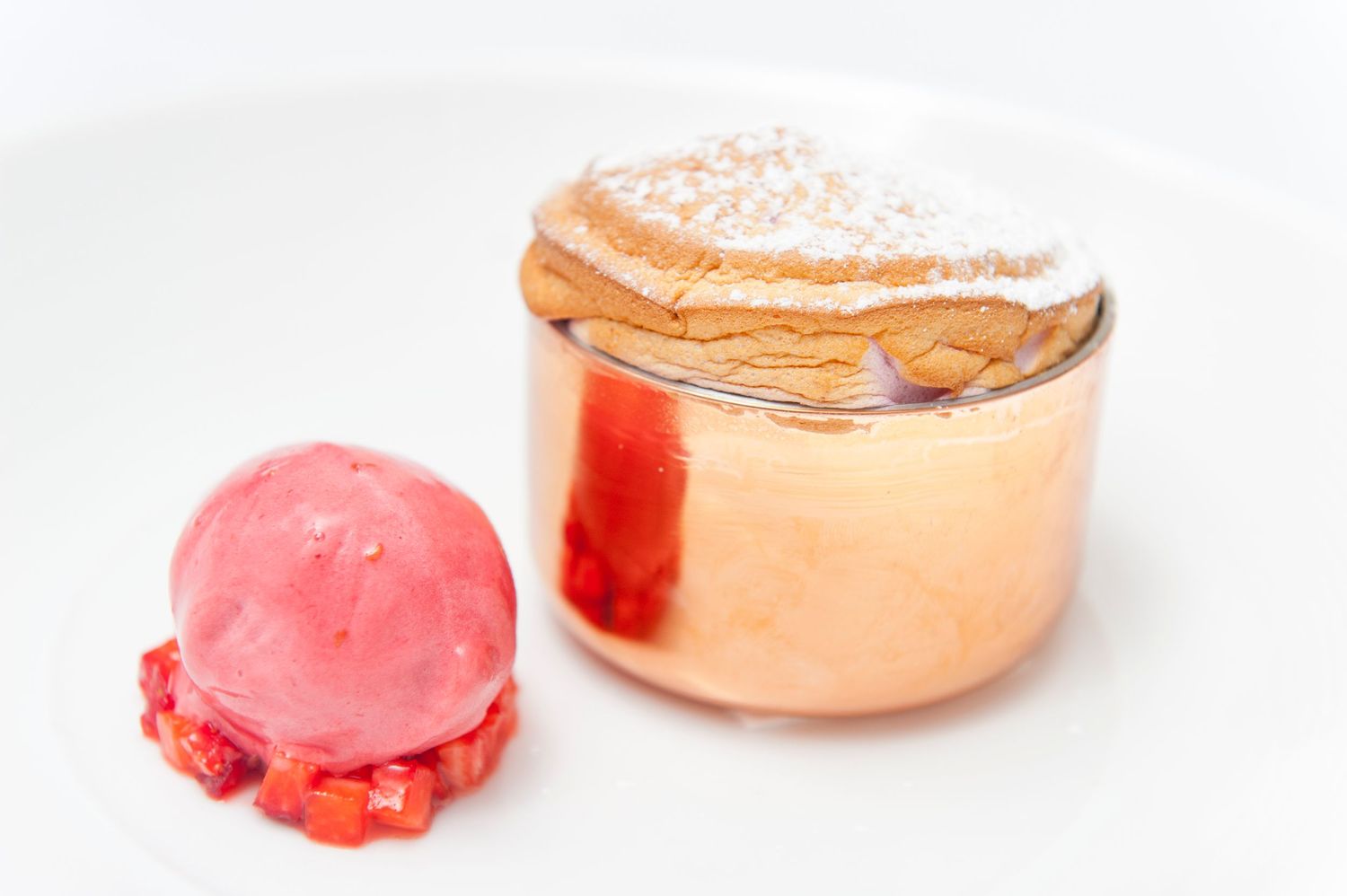 Elegant plated dessert with pink sorbet and powdered sugar dusted pastry on white dish.