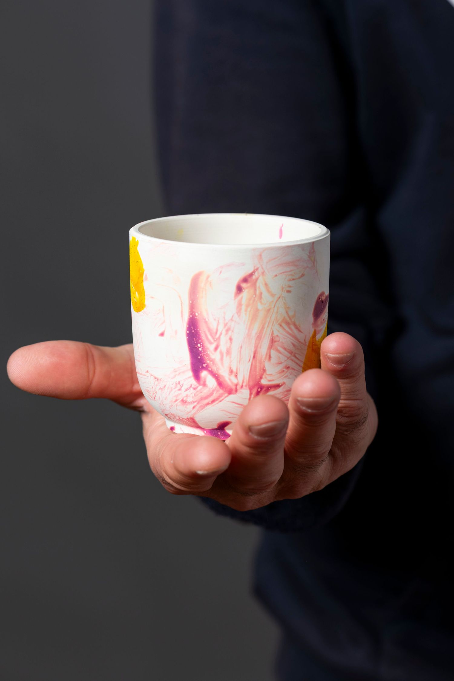 Four sequential photos show hands holding a white ceramic cup with pink and yellow artistic designs against a dark background.