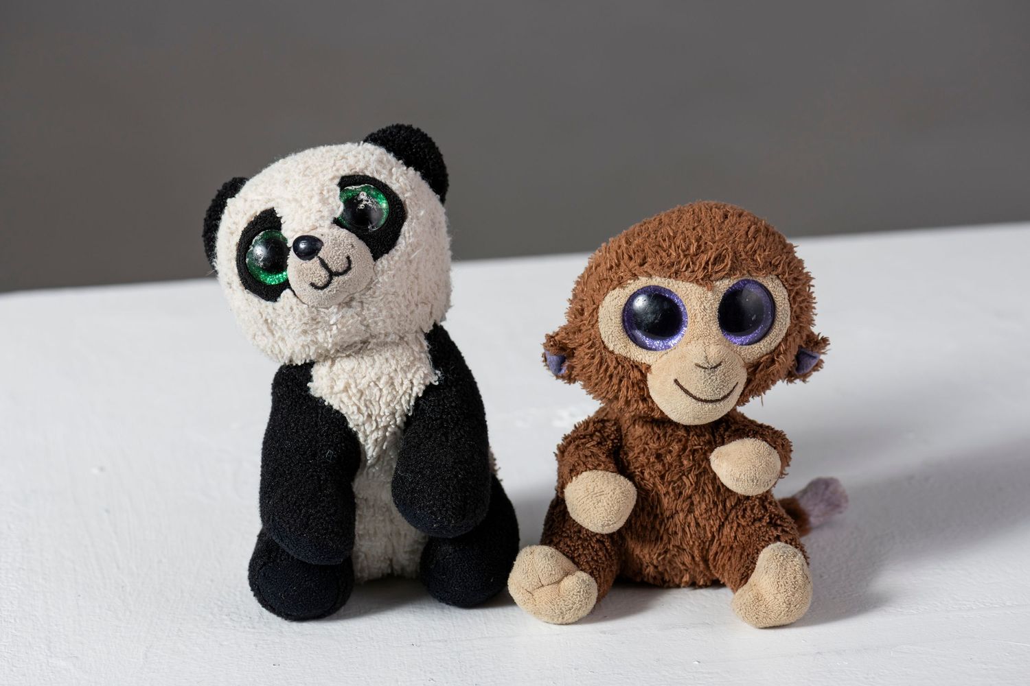 Small plush toys featuring pandas and monkeys arranged in a row on a white surface.