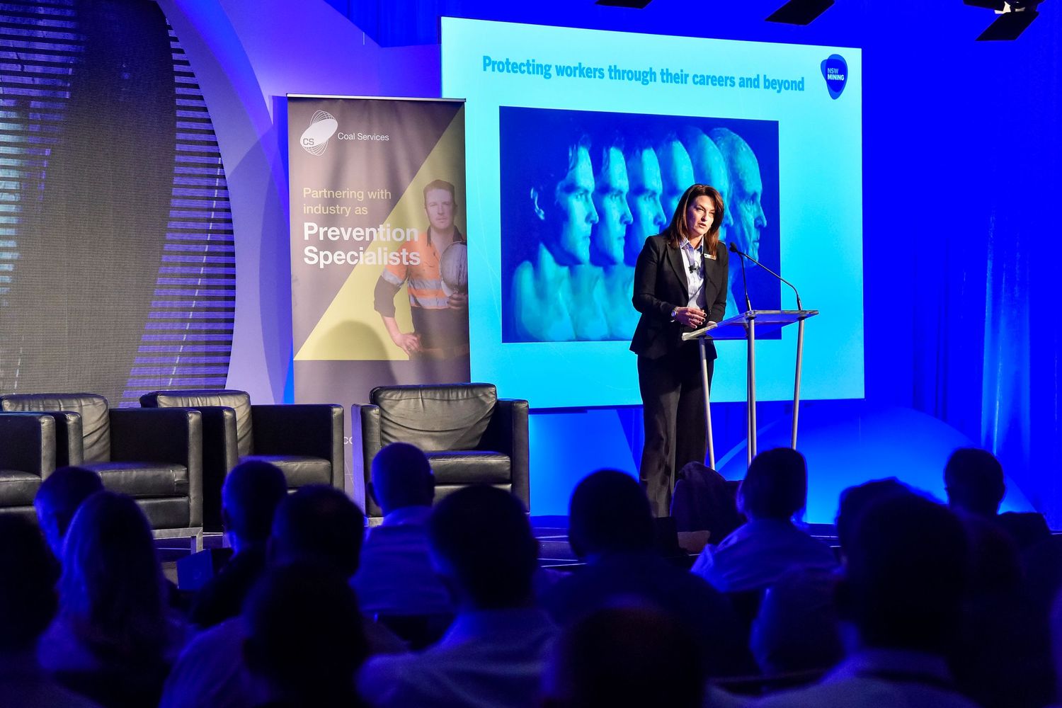Corporate presentation with digital displays showing business graphics in blue-lit auditorium.