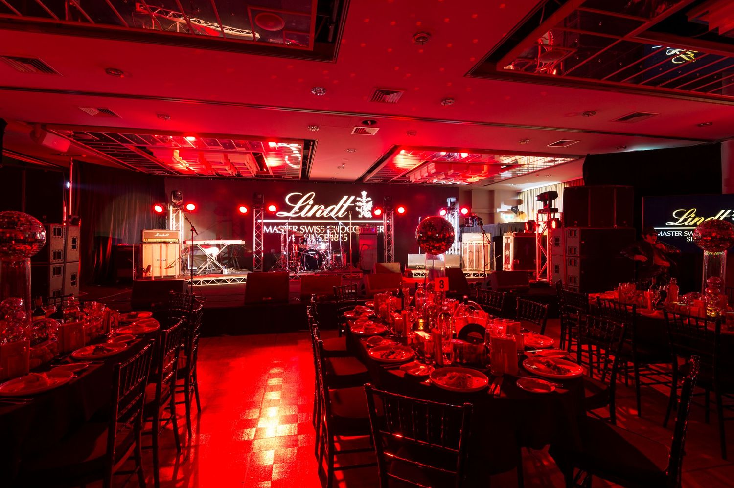 Nightclub interior bathed in dramatic red lighting shows empty dance floor and seating areas from multiple angles.
