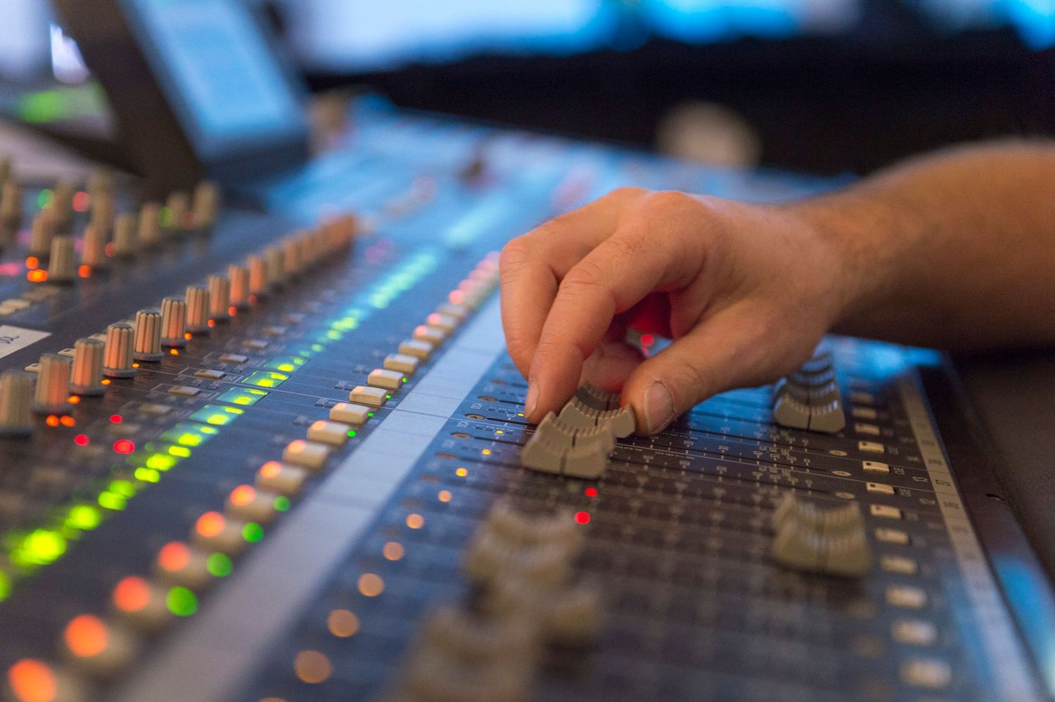 Professional audio mixing console with colorful LED lights and faders being operated in a recording studio.