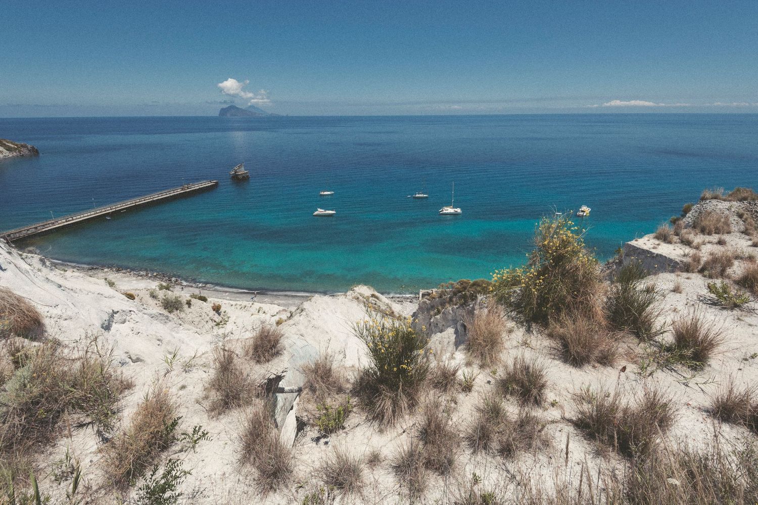 Panoramic view of turquoise ocean waters and sandy dunes along a pristine coastline on a sunny day.