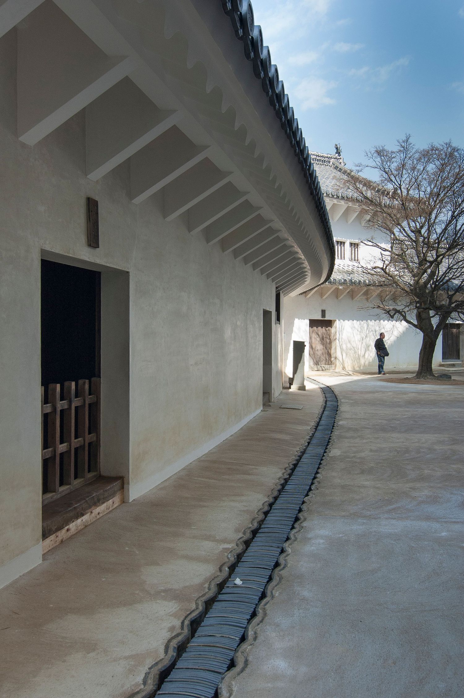 Long covered walkway with traditional Japanese architecture featuring white walls and dark wooden beams.