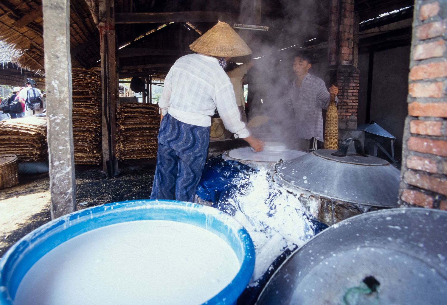 Large vats of boiling water create steam in an industrial food preparation facility.