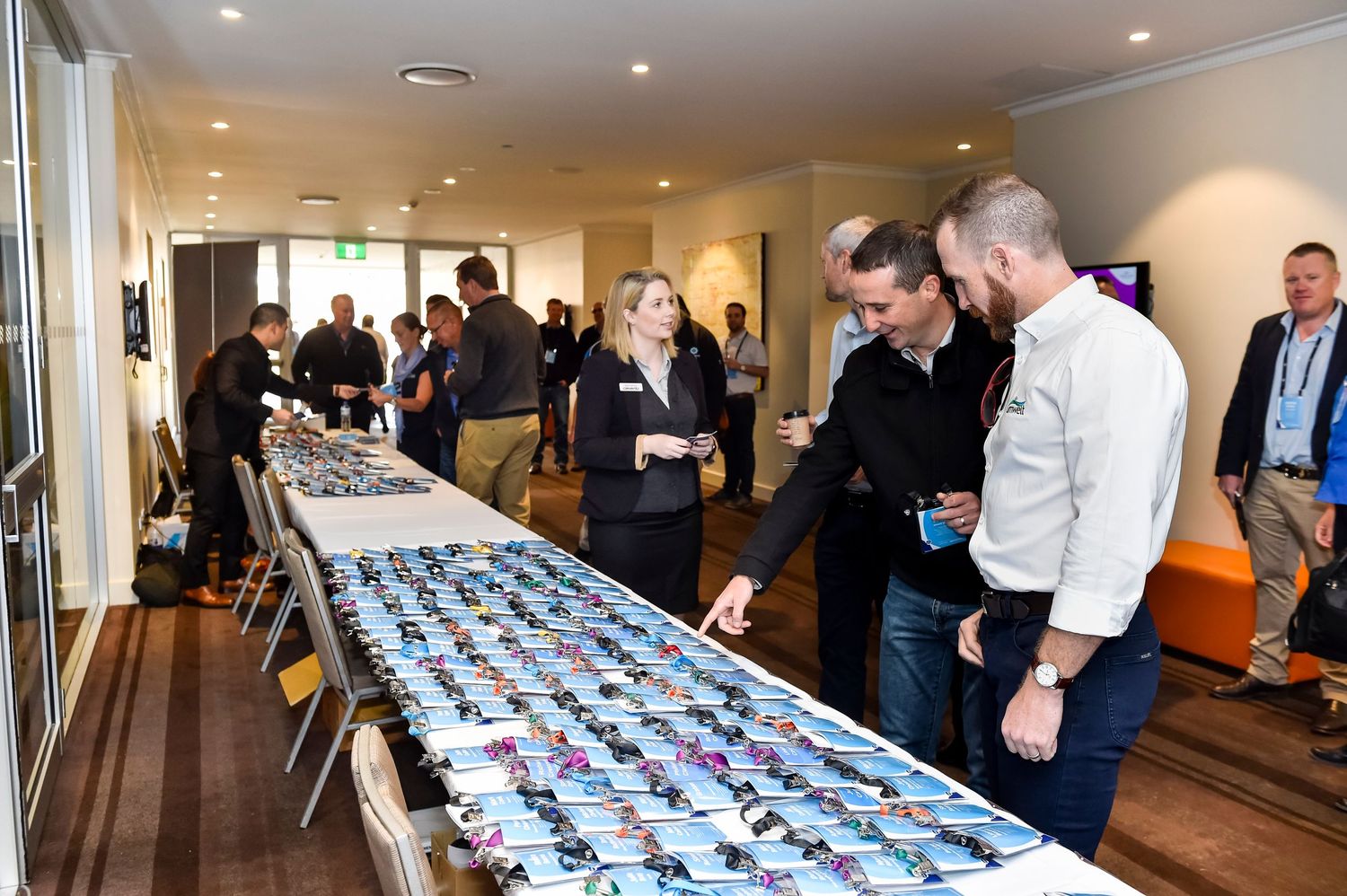 Conference attendees gather around the registration desk in a brightly lit venue.