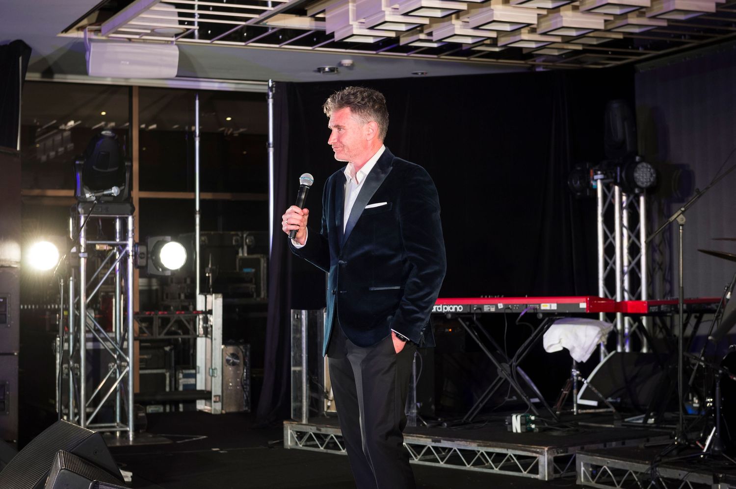 Stage lighting equipment and truss rigging systems are visible in a dark performance venue setting.