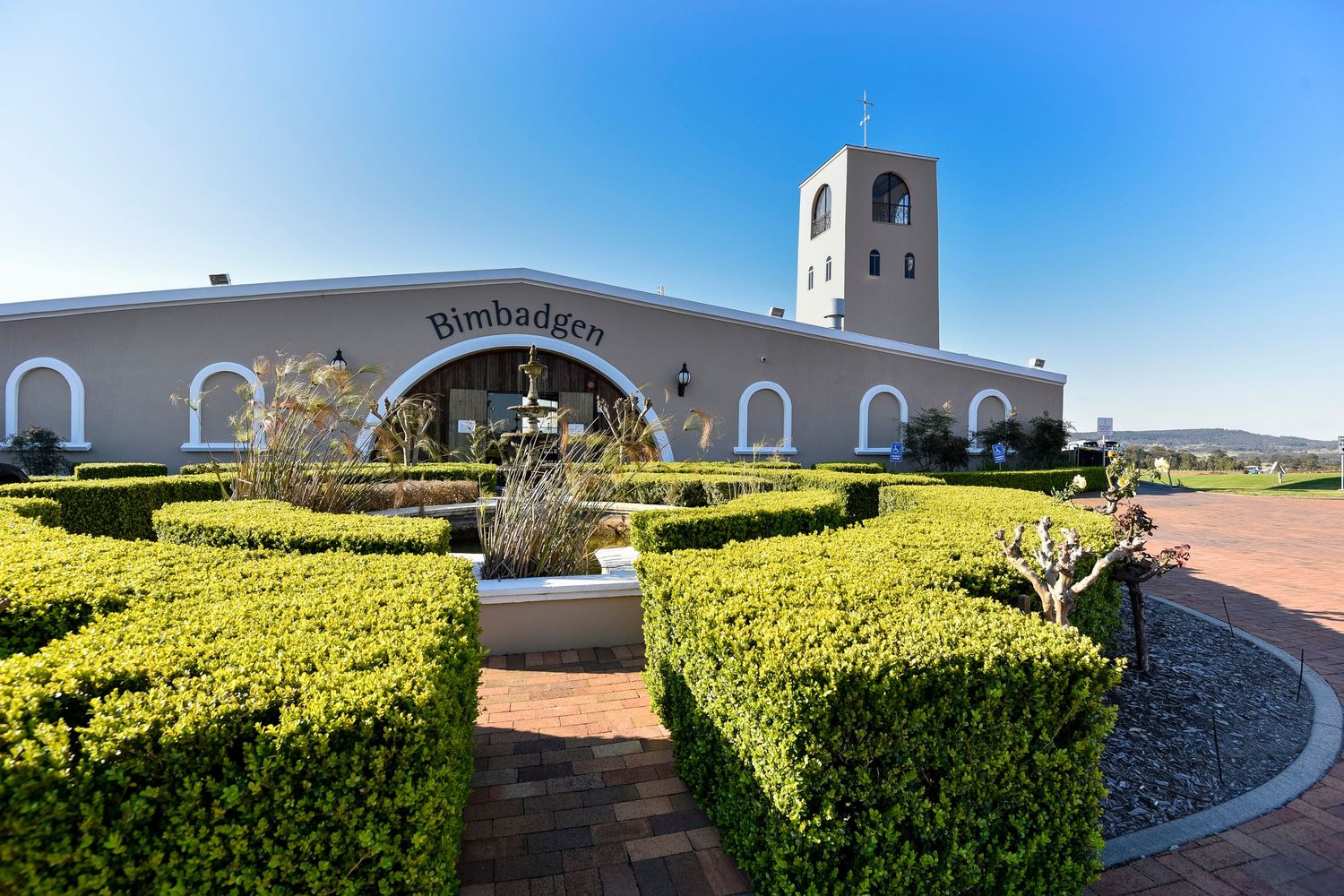 White mission-style building with manicured hedges under bright blue sky on Bimbadgen winery in the Hunter Valley.