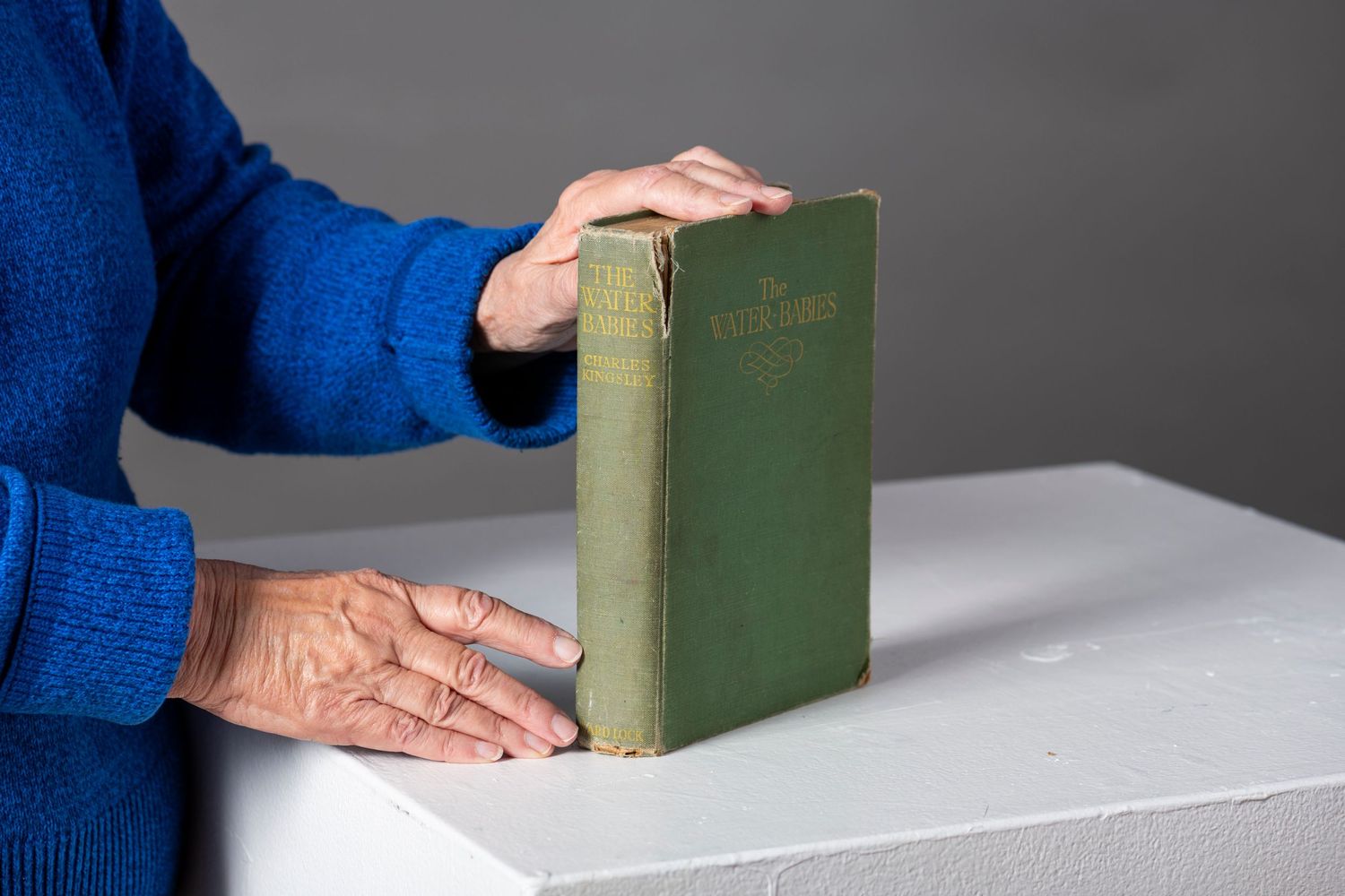 A pair of hands demonstrating the process of opening and closing a vintage green hardcover book on a white surface.