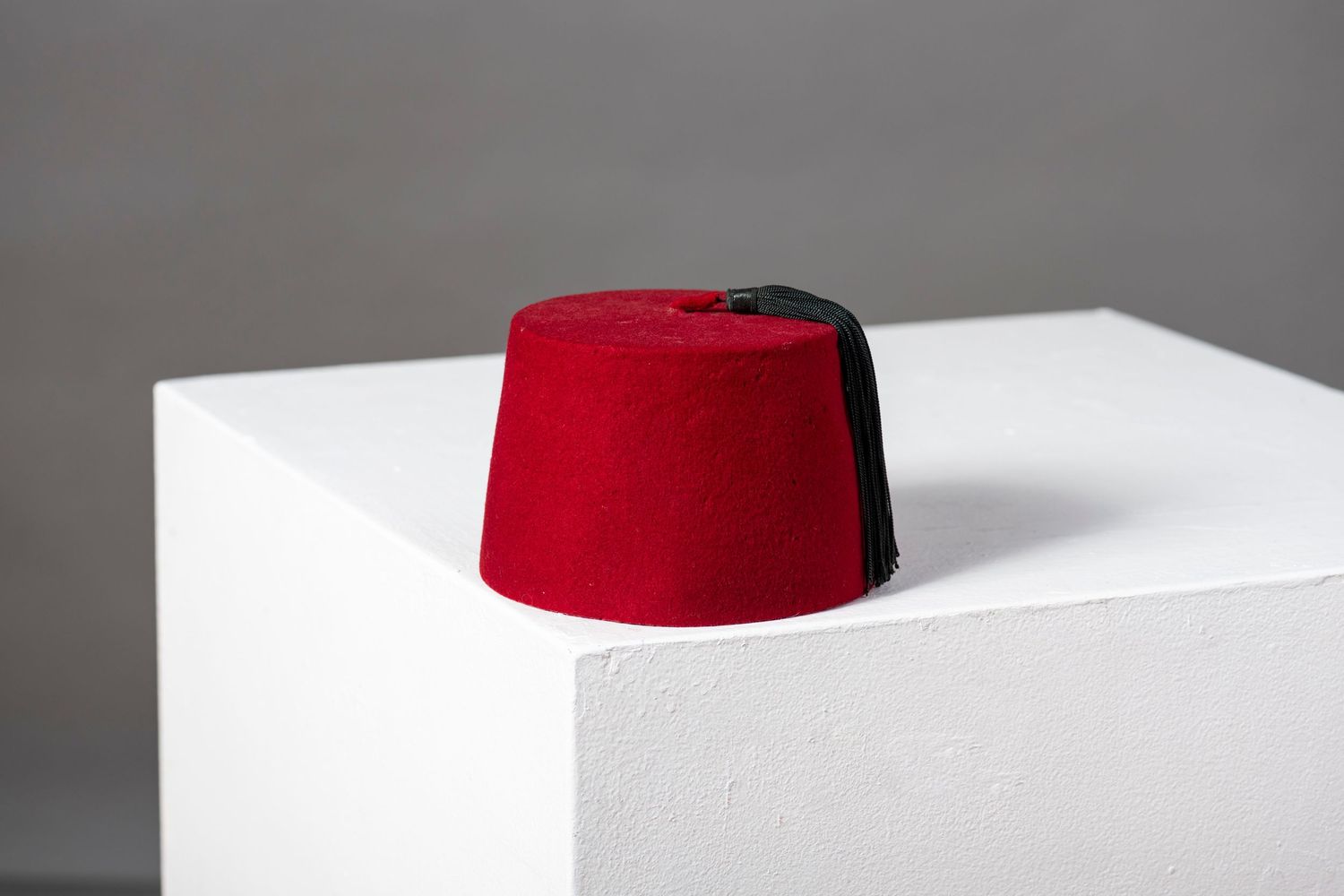 A red fez hat shown from multiple angles on a white surface against a gray background.