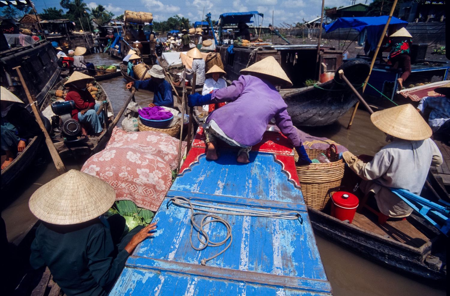 Aerial view of boats with blue tarps lined up at a bustling floating market.