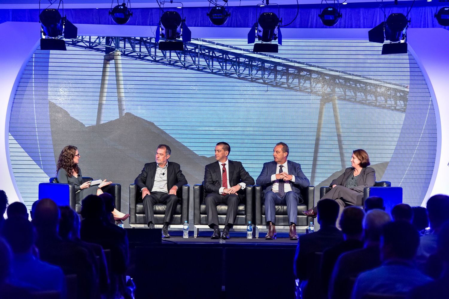 Wide stage setup with professional lighting rigs and multiple presentation screens at business event.