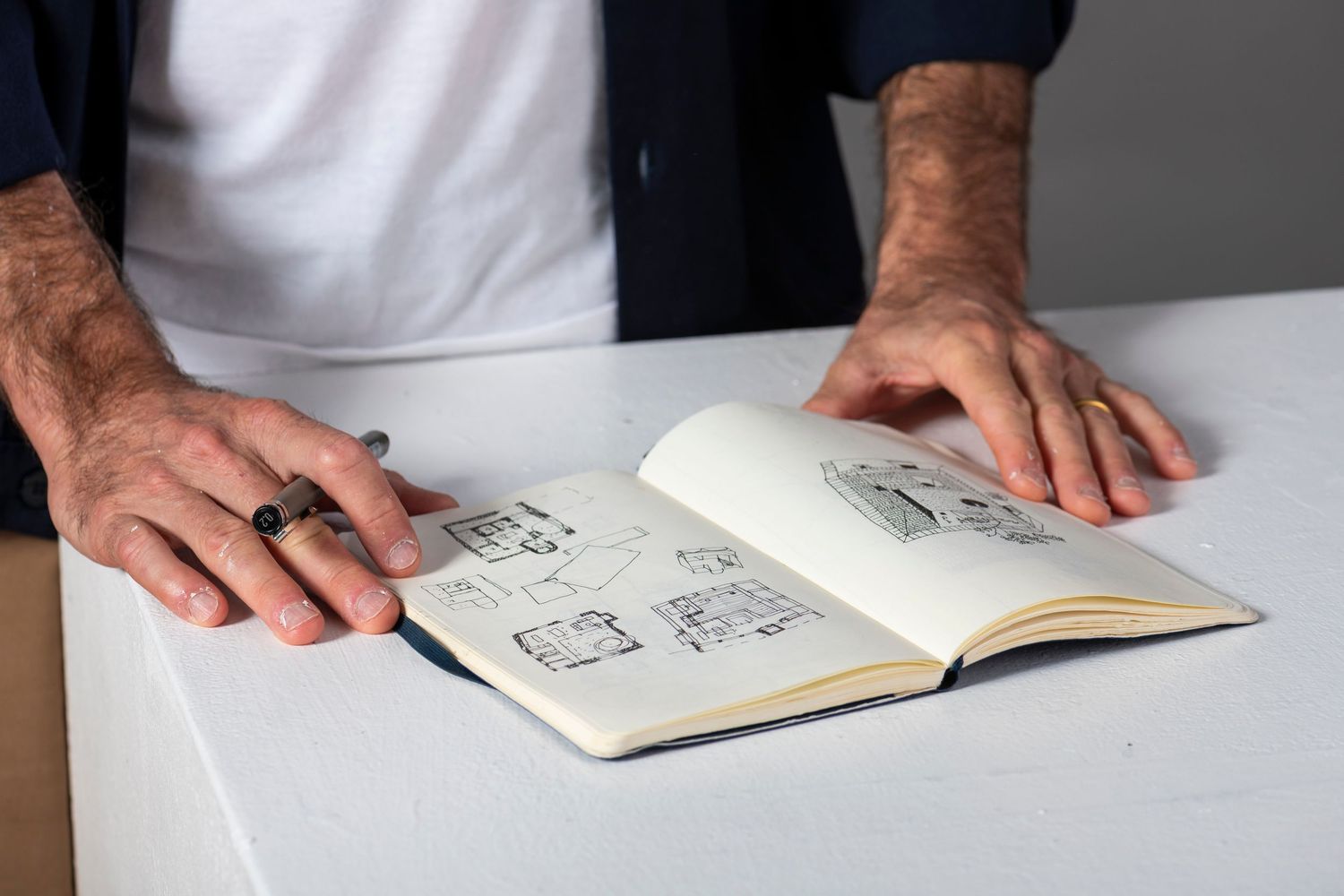 Hands shown writing or drawing in an open notebook on a white surface.