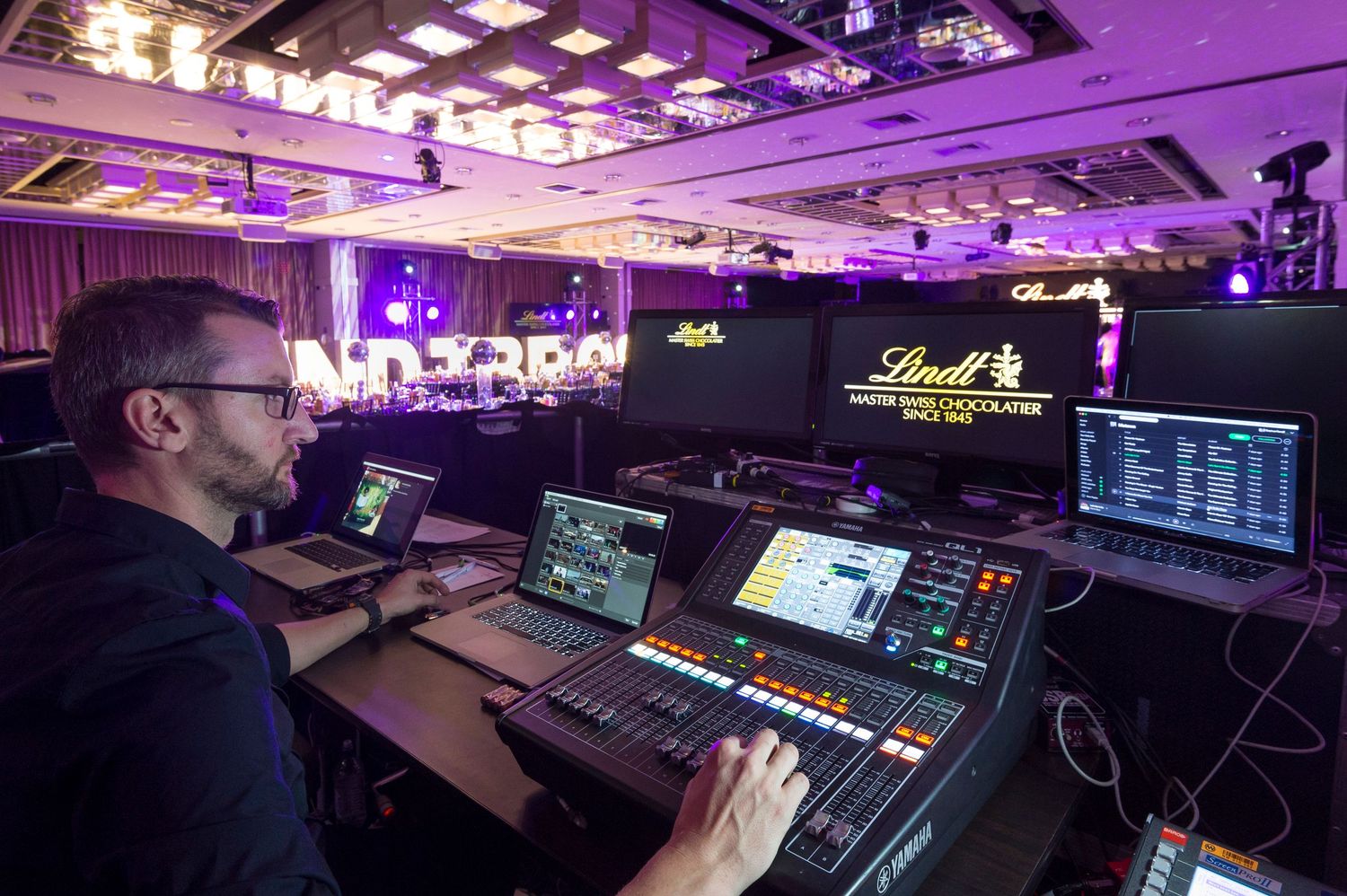 Professional control room with purple lighting shows multiple monitors and production equipment for live event broadcasting.